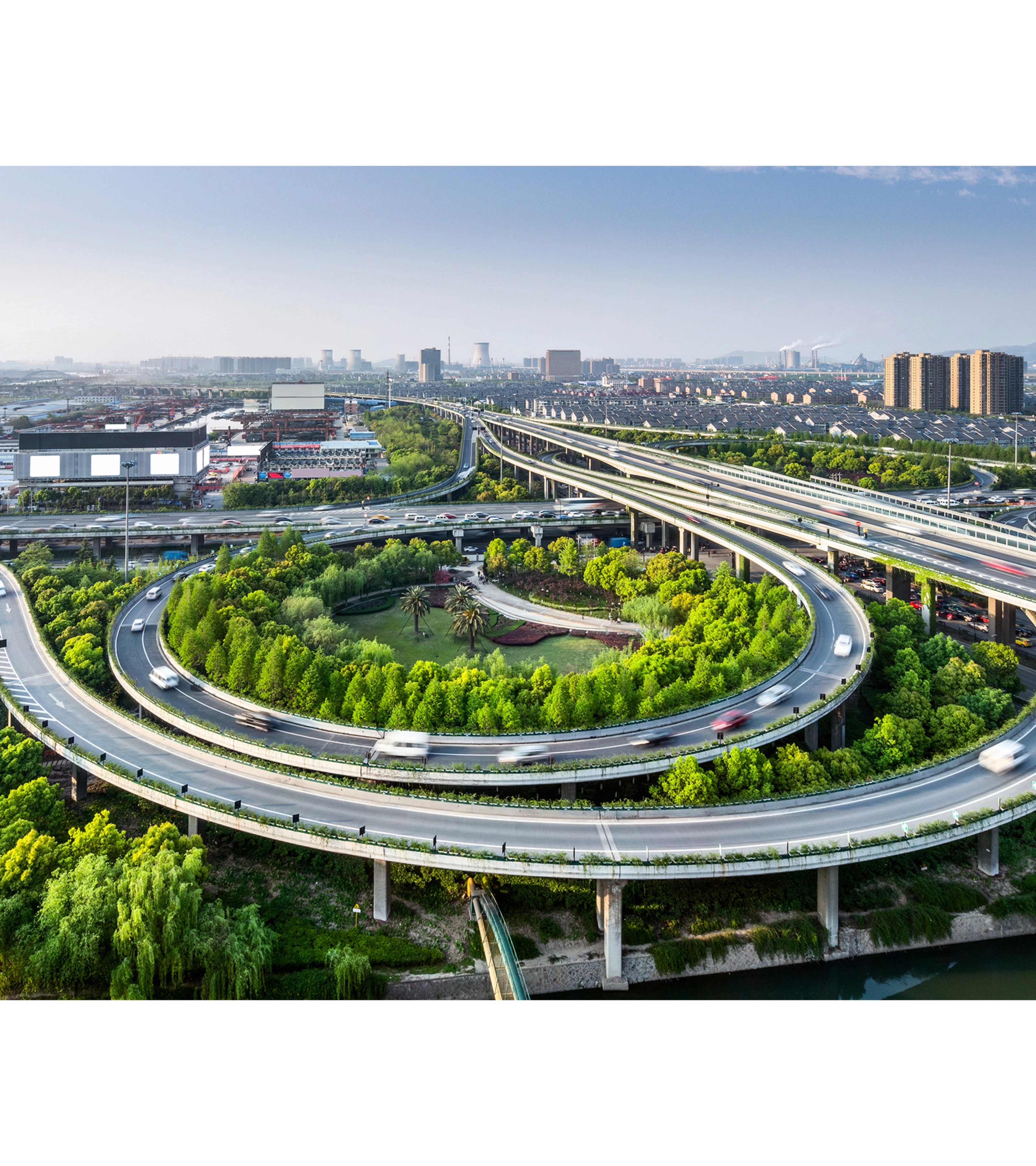 Large highway interchange with loop ramps and green areas in an urban cityscape.