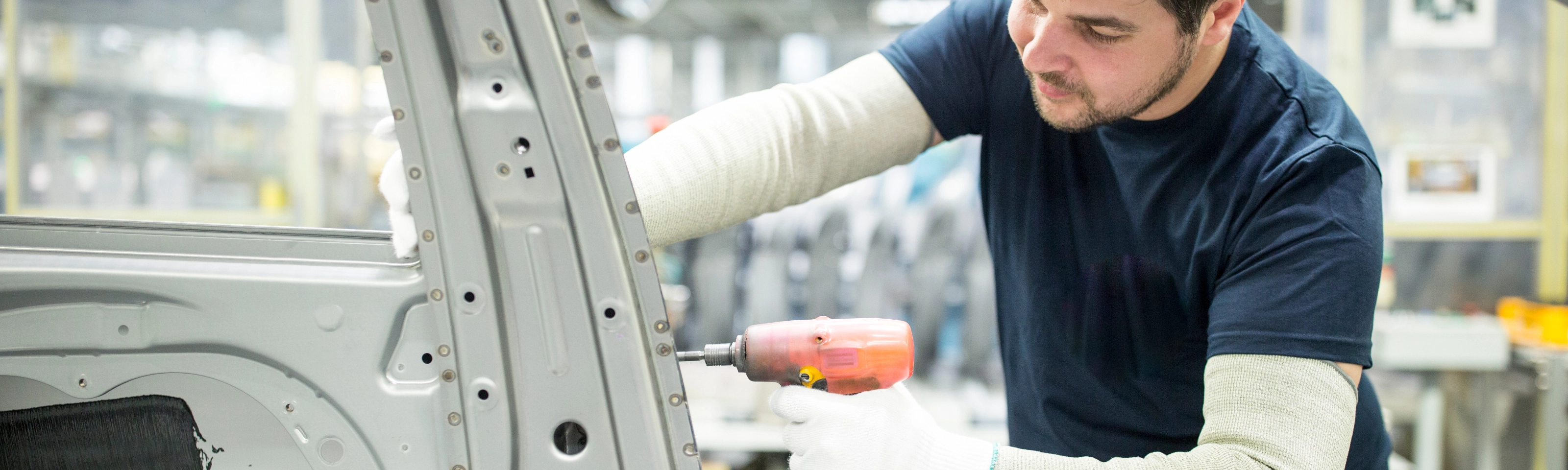 Arbeiter bearbeitet mit einem Elektrowerkzeug eine Autokarosserie in moderner Fabrik.