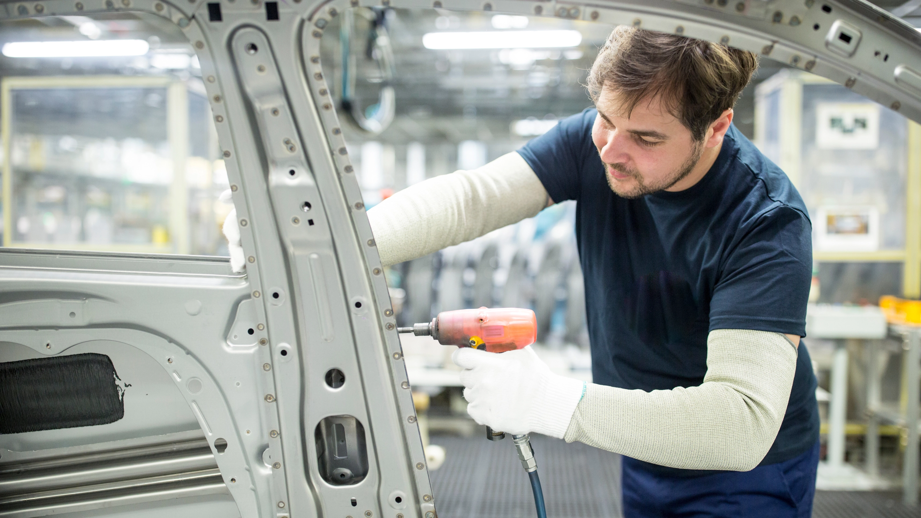 Arbeiter bearbeitet mit einem Elektrowerkzeug eine Autokarosserie in moderner Fabrik.