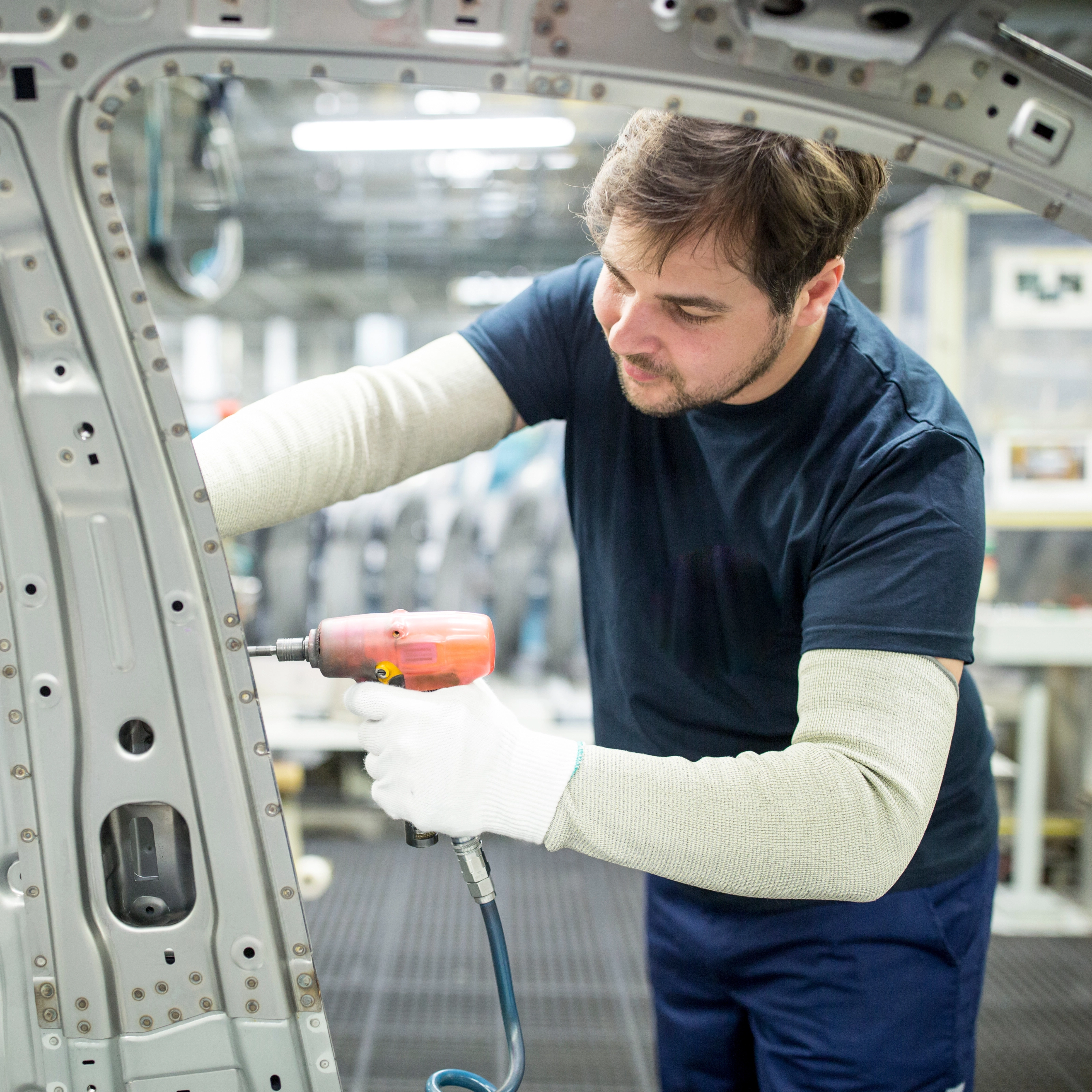 Arbeiter bearbeitet mit einem Elektrowerkzeug eine Autokarosserie in moderner Fabrik.
