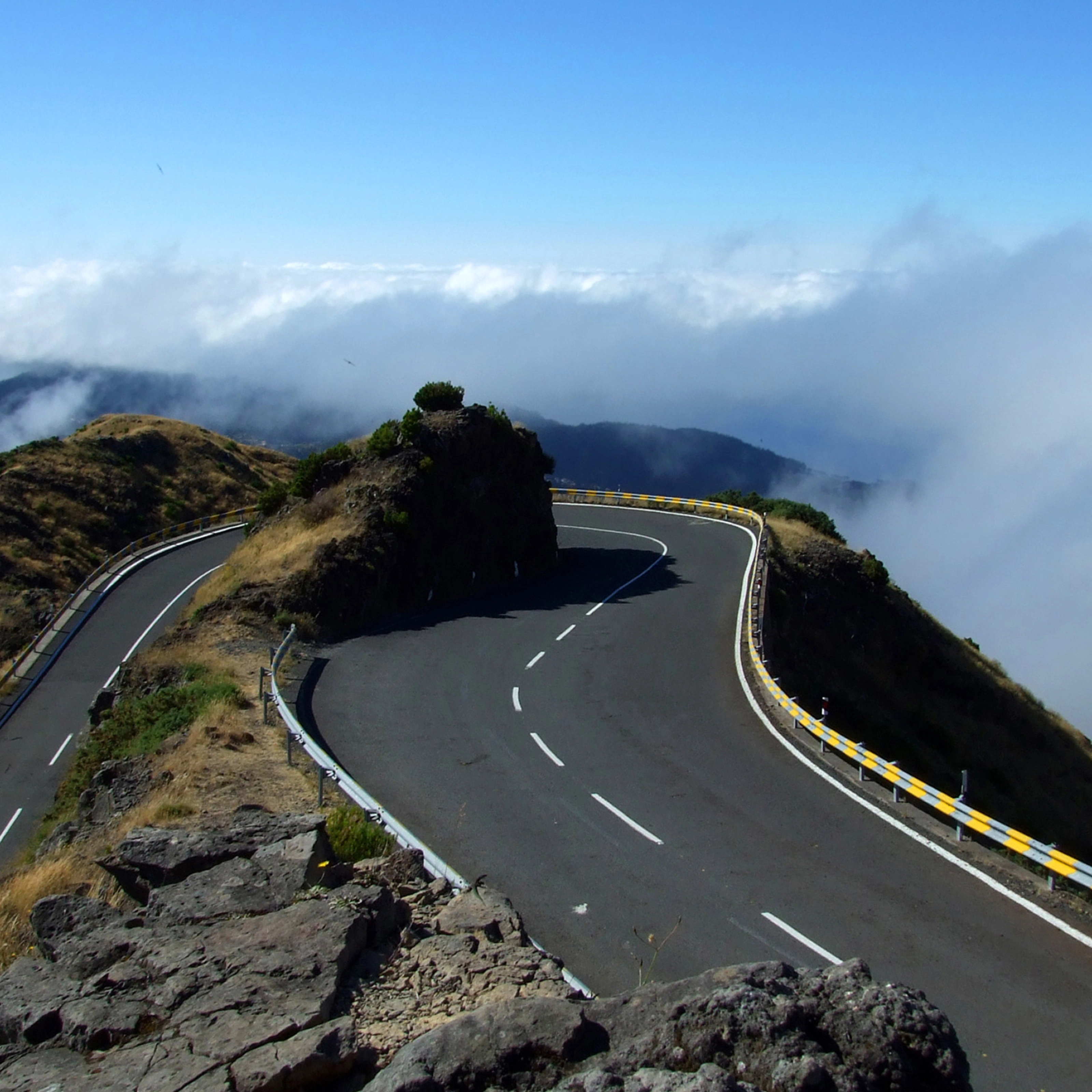 Kurvige Bergstraße mit Leitplanken und nebligem Wolkenhintergrund.