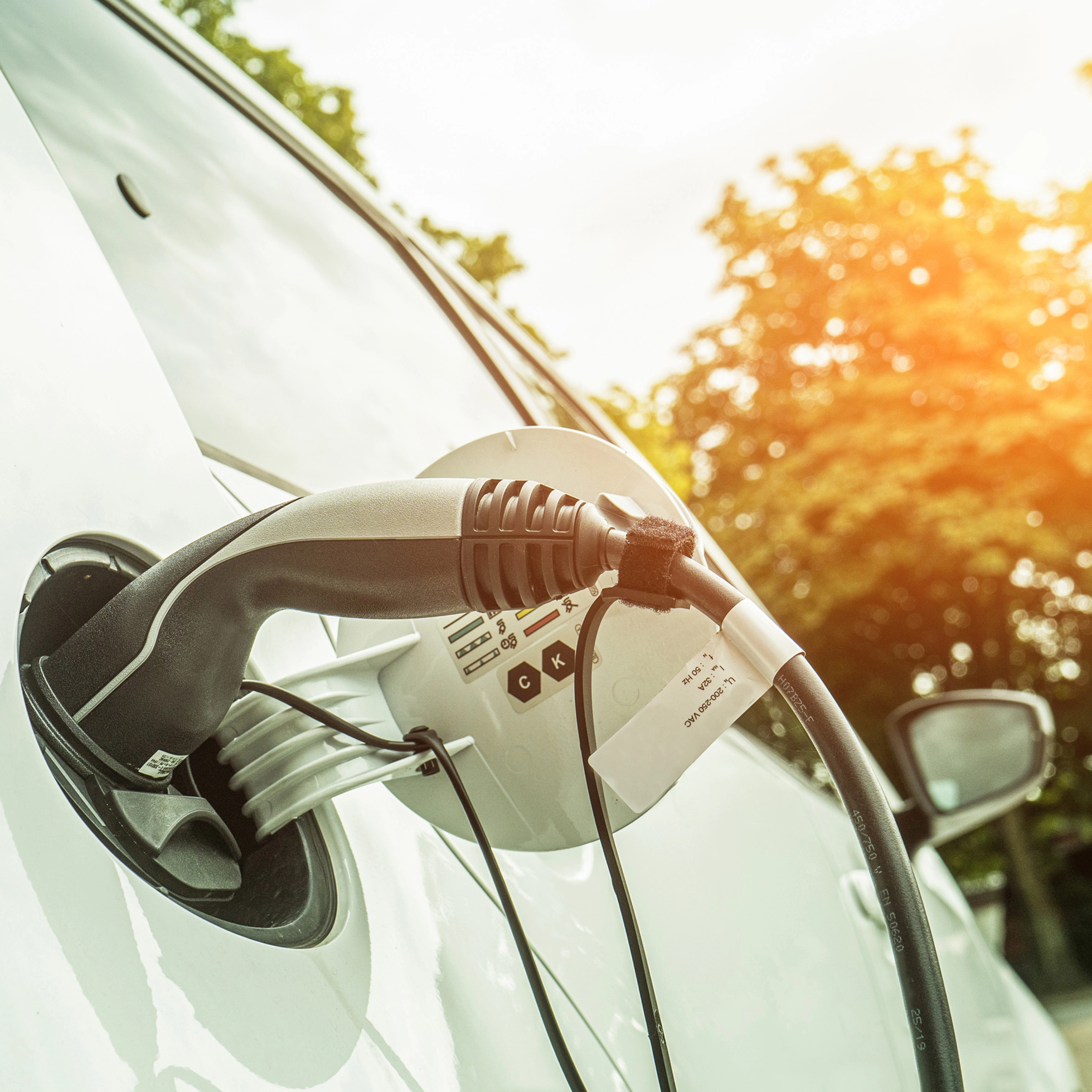 Electric car charging outdoors in sunlight, with cable plugged into the side of the vehicle.