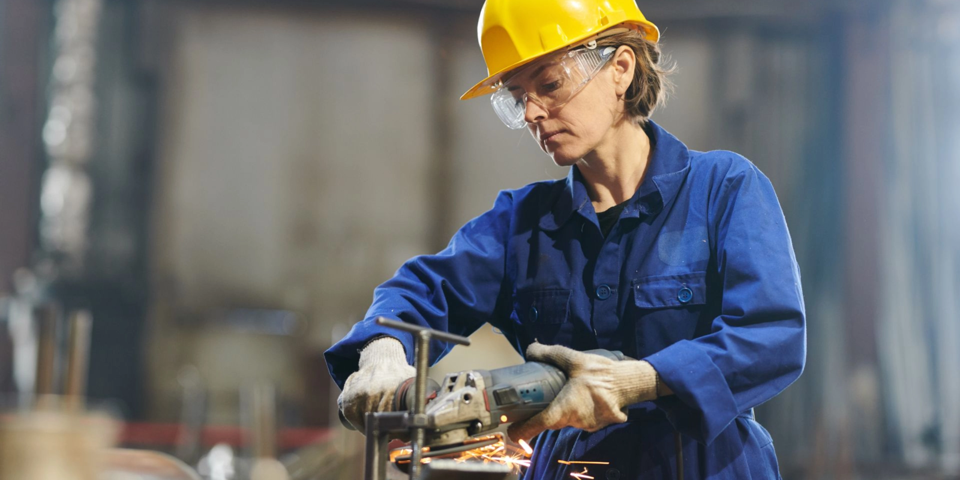 A woman works on a metal workpiece with an angle grinder