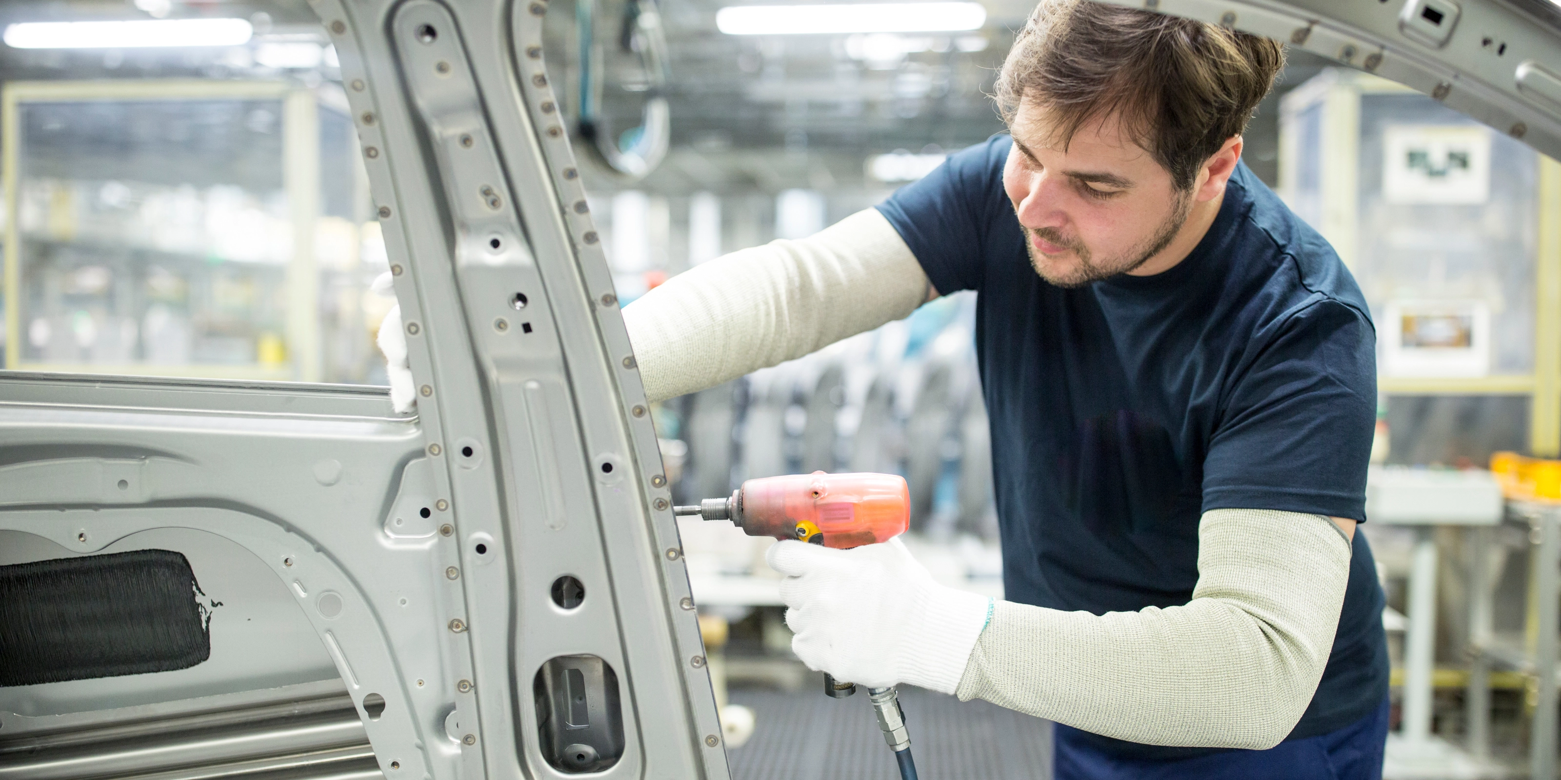 Arbeiter bearbeitet mit einem Elektrowerkzeug eine Autokarosserie in moderner Fabrik.