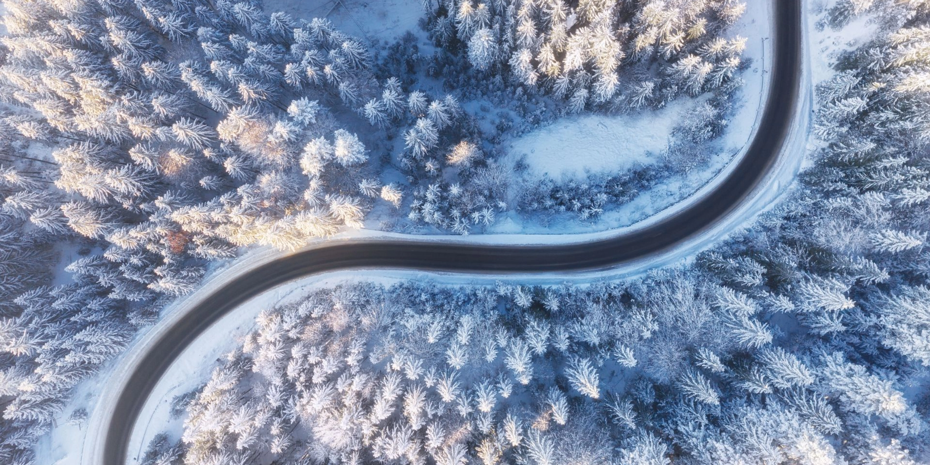 Kurvige Straße verläuft durch einen verschneiten Wald aus der Vogelperspektive.