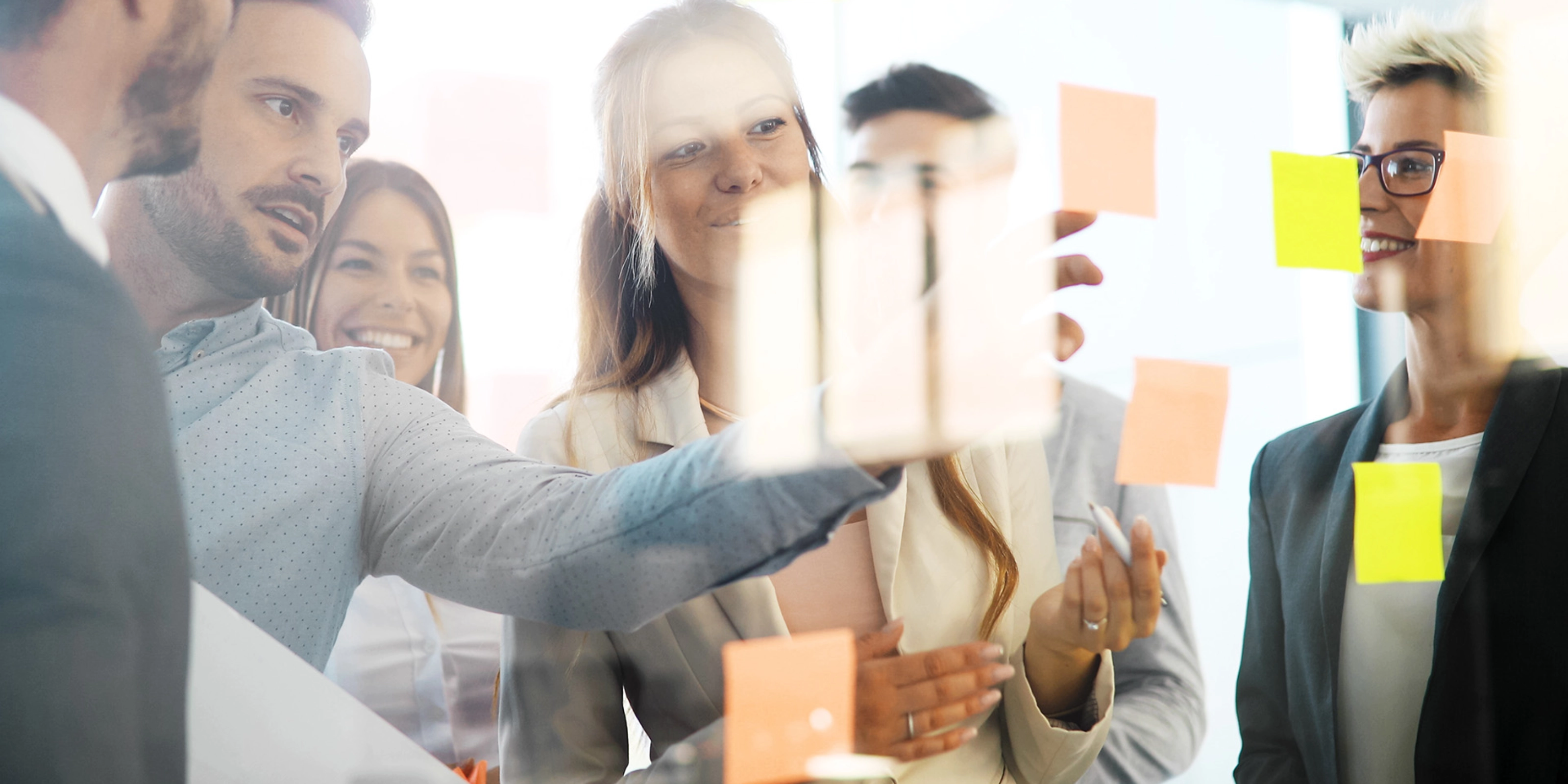 Group of people planning together in front of a glass wall with colorful sticky notes.