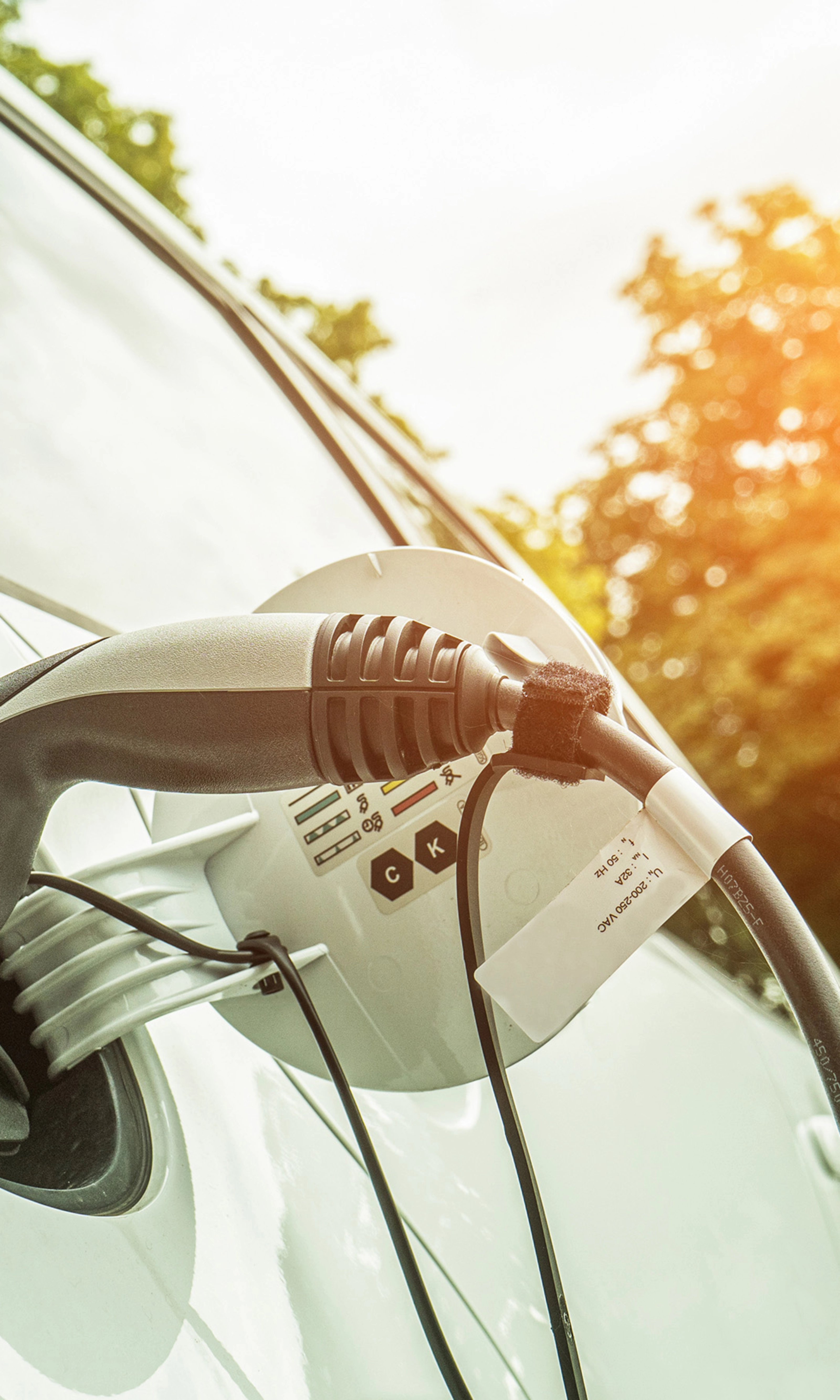 Electric car charging outdoors in sunlight, with cable plugged into the side of the vehicle.