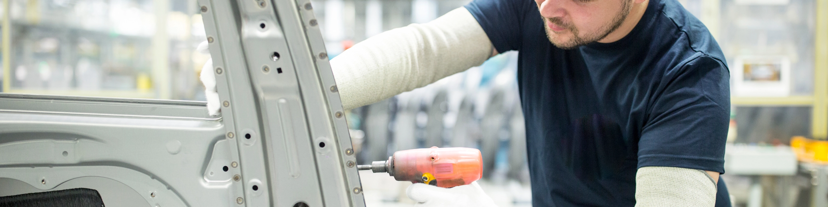 Arbeiter bearbeitet mit einem Elektrowerkzeug eine Autokarosserie in moderner Fabrik.