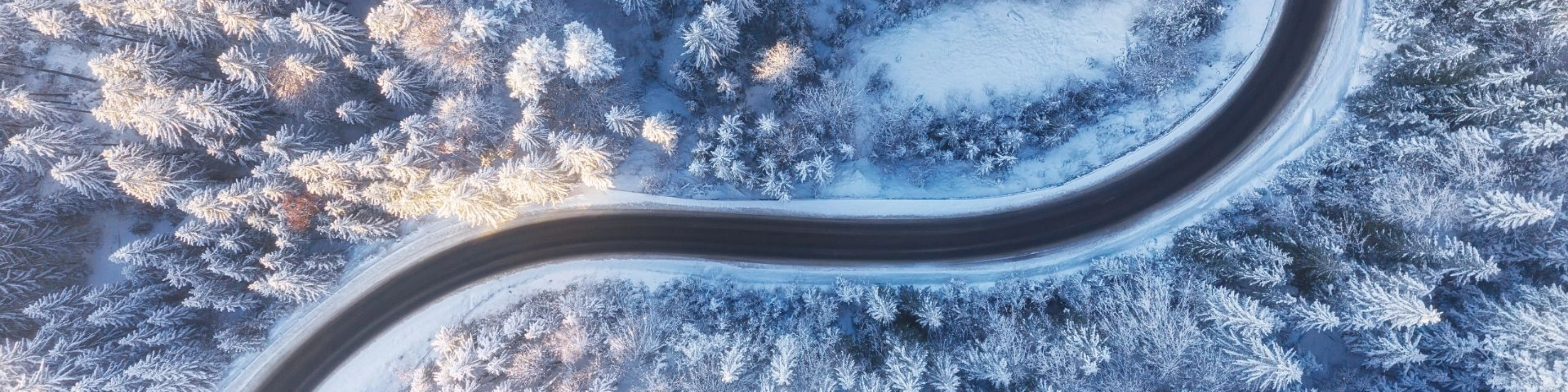 Kurvige Straße verläuft durch einen verschneiten Wald aus der Vogelperspektive.