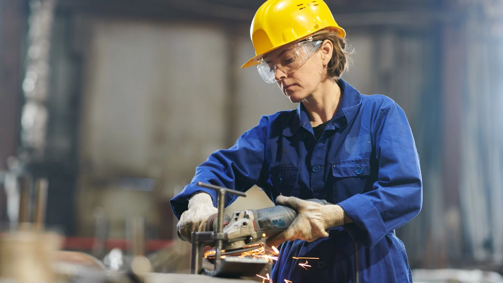 A woman works on a metal workpiece with an angle grinder