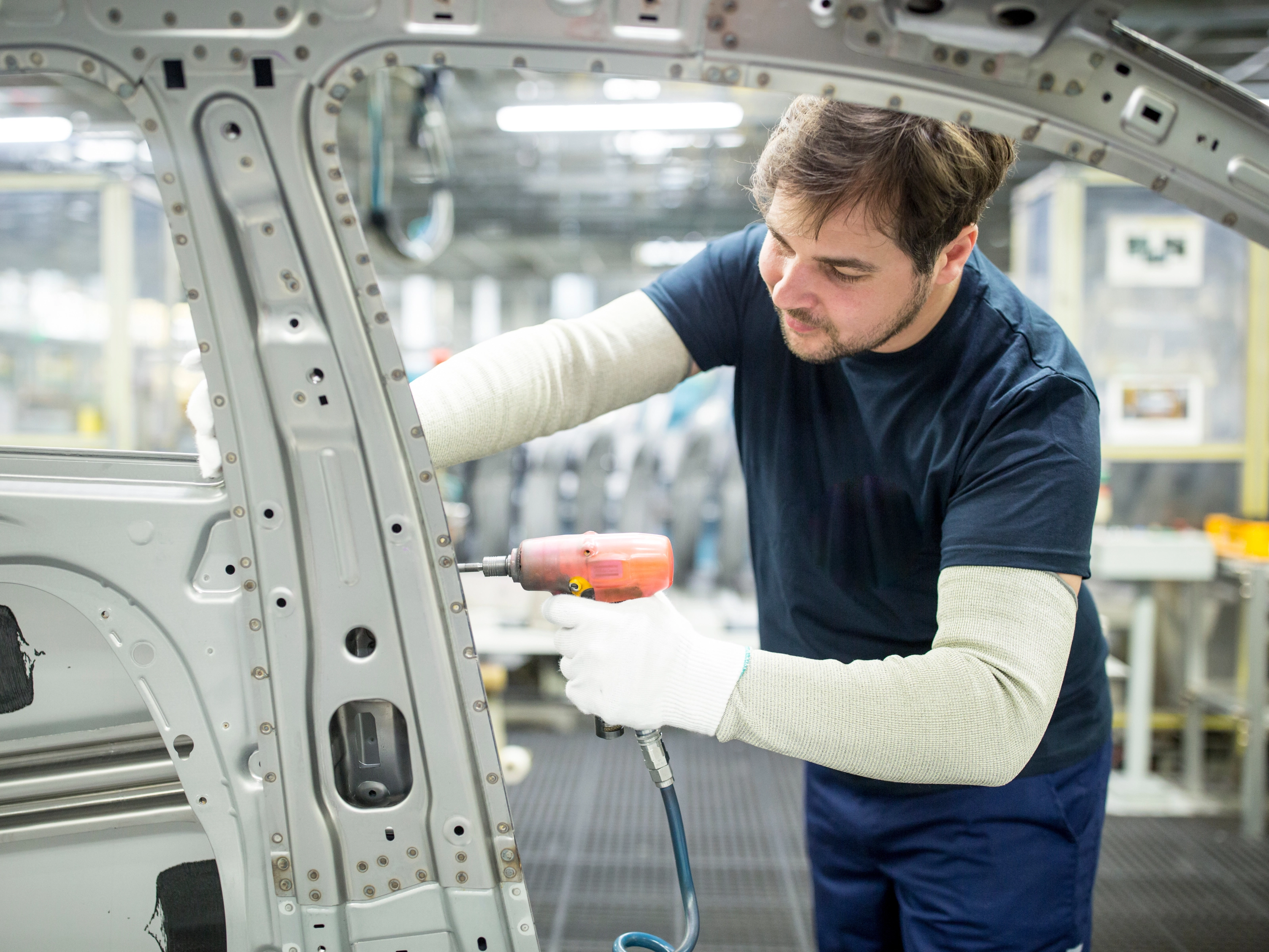 Arbeiter bearbeitet mit einem Elektrowerkzeug eine Autokarosserie in moderner Fabrik.