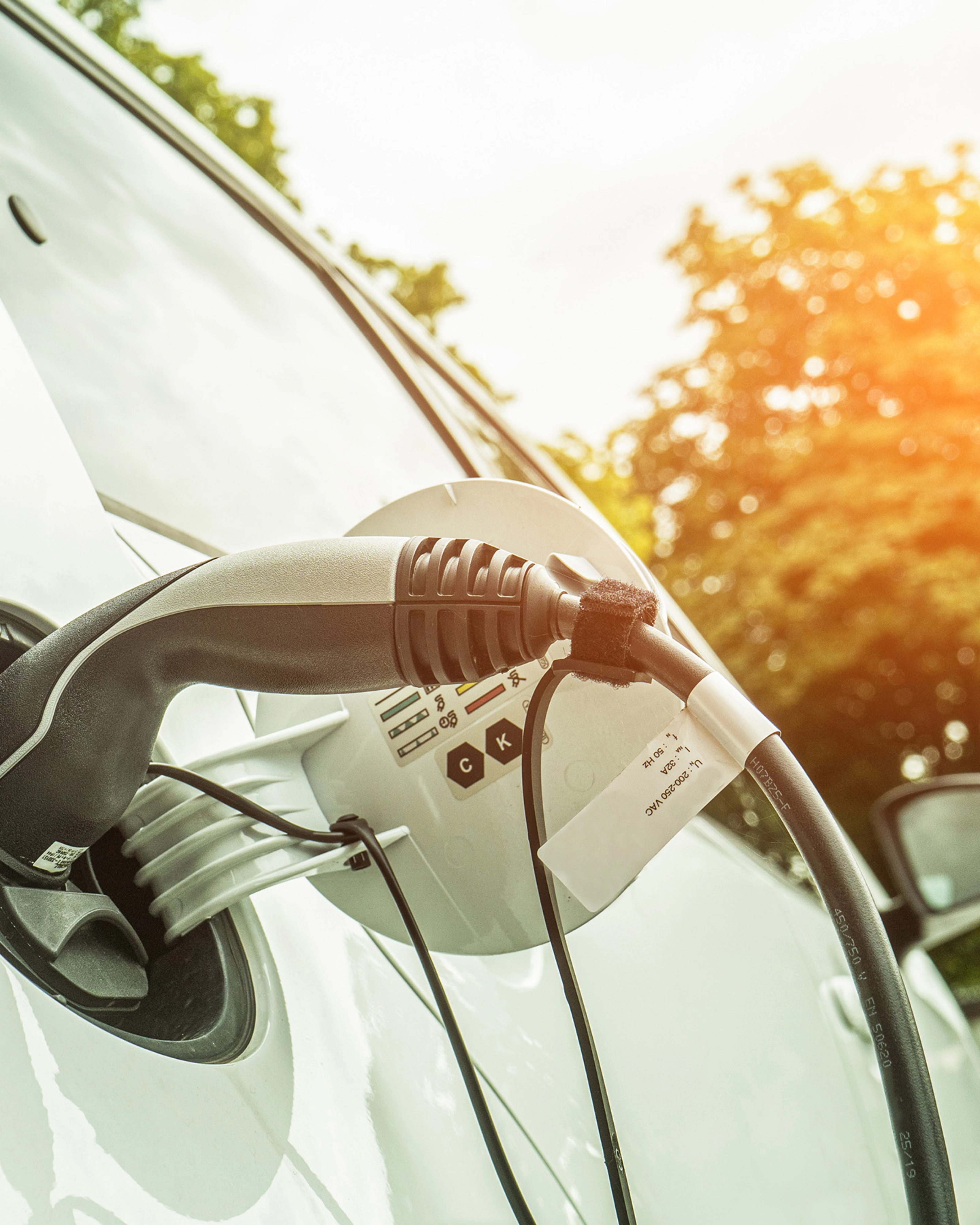 Electric car charging outdoors in sunlight, with cable plugged into the side of the vehicle.