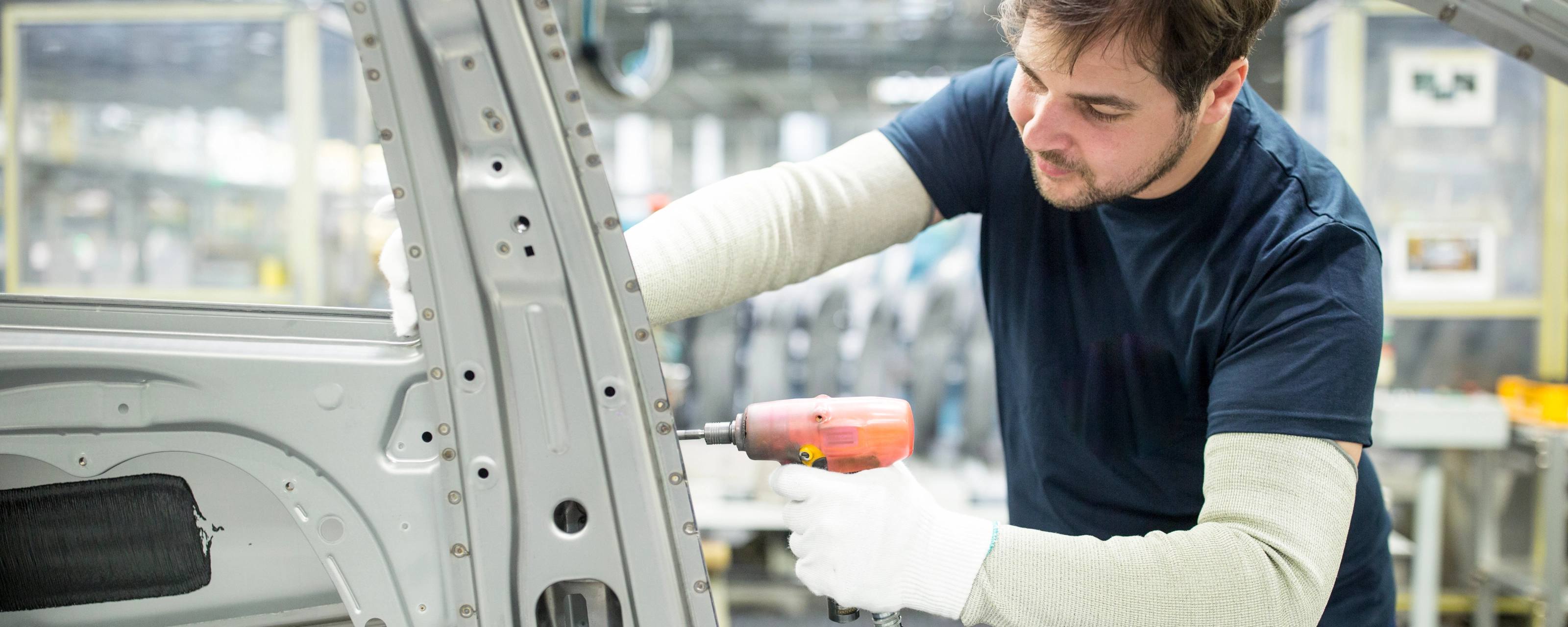 Arbeiter bearbeitet mit einem Elektrowerkzeug eine Autokarosserie in moderner Fabrik.