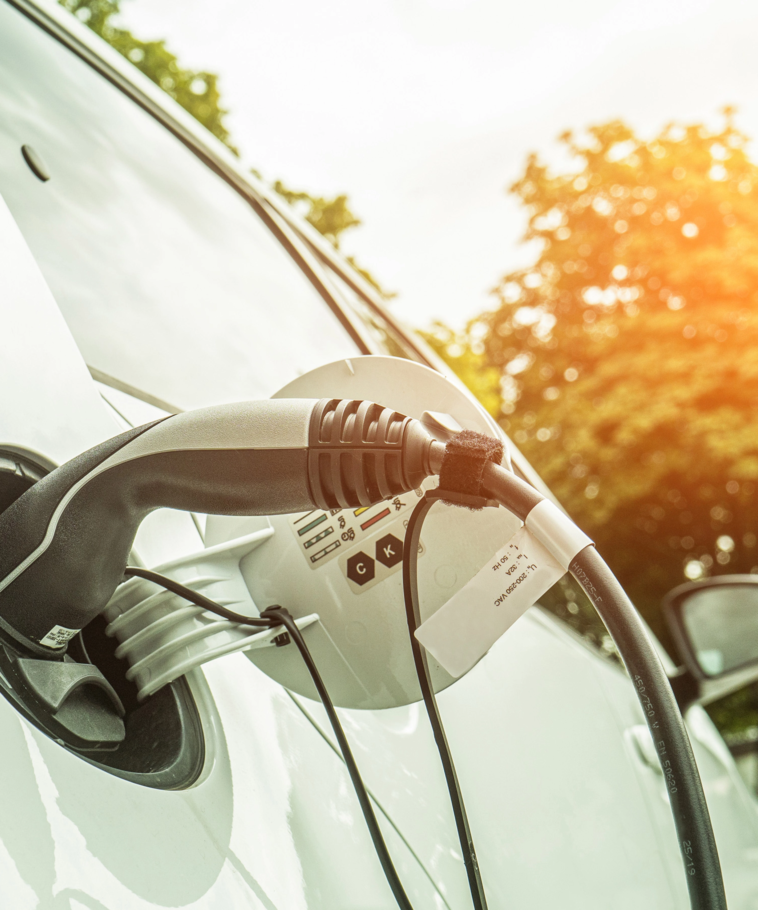 Electric car charging outdoors in sunlight, with cable plugged into the side of the vehicle.