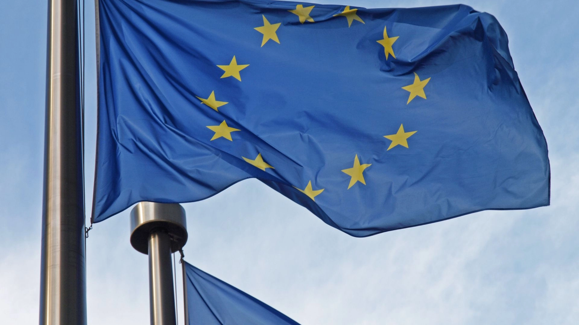 EU-Flagge weht an einem Fahnenmast vor hellblauem Himmel.