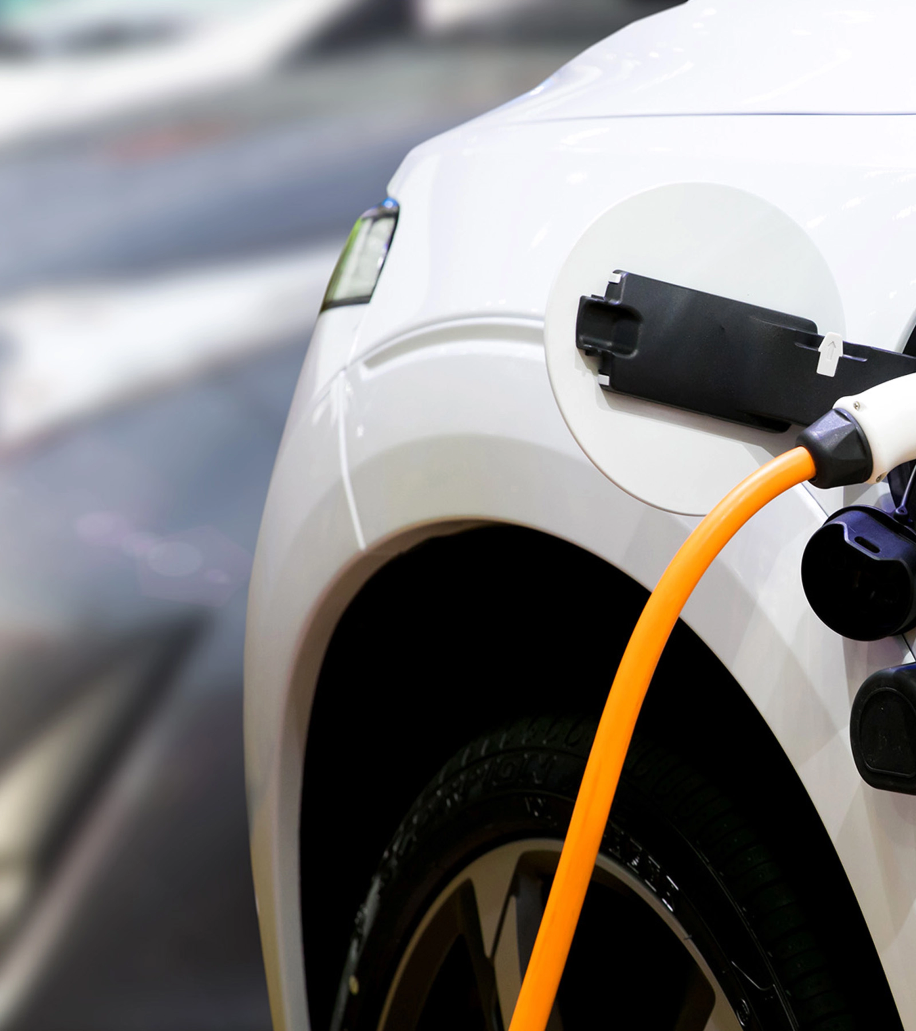 Nahaufnahme eines Elektroautos, das mit einem orangefarbenen Kabel geladen wird.