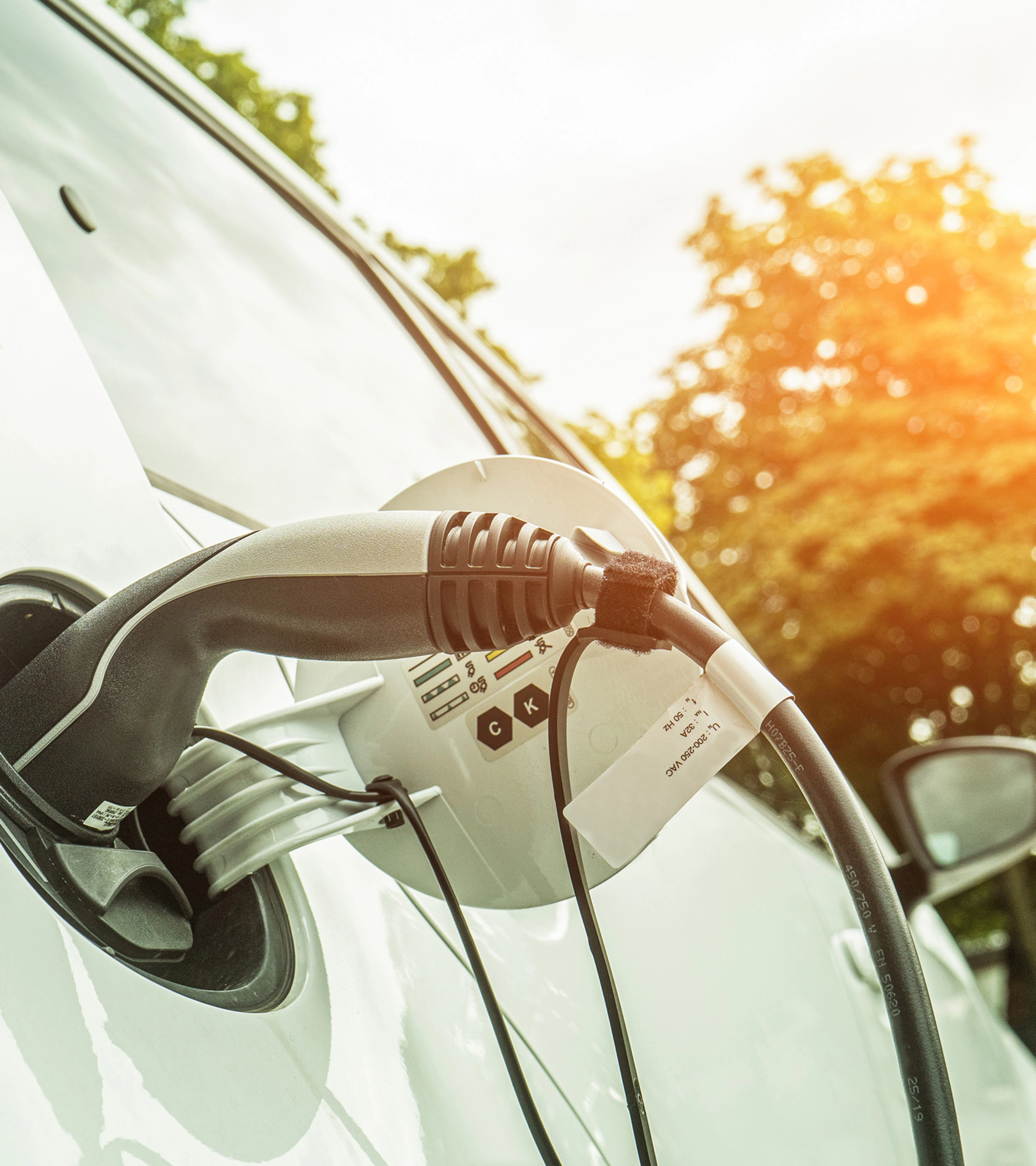 Electric car charging outdoors in sunlight, with cable plugged into the side of the vehicle.