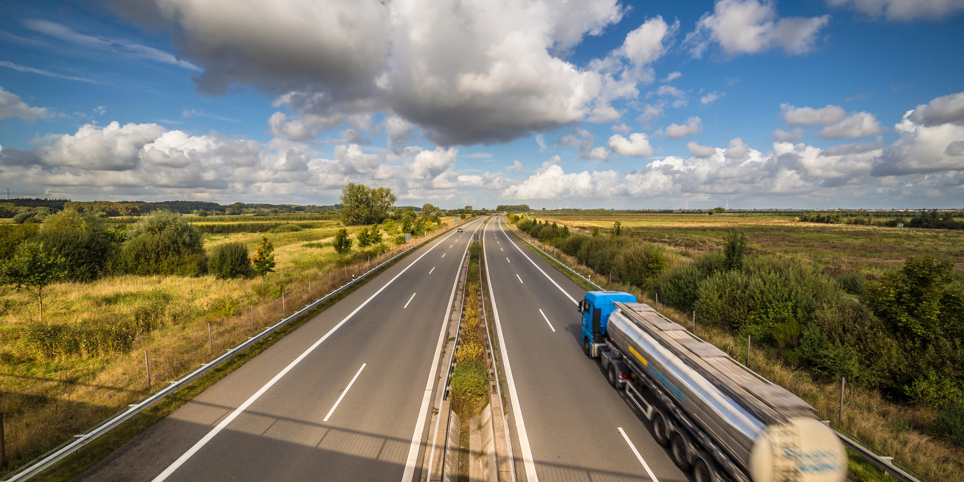 Tanklastwagen auf ländlicher Autobahn unter leicht bewölktem Himmel.