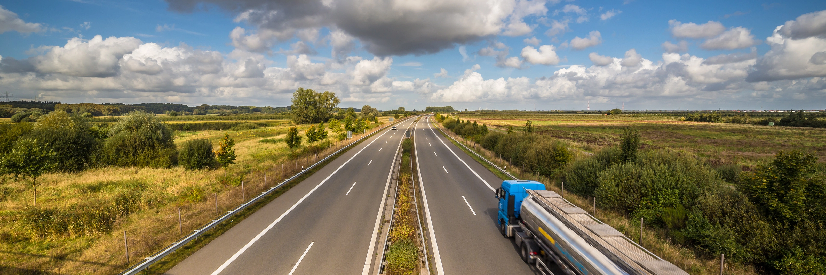 Tanklastwagen auf ländlicher Autobahn unter leicht bewölktem Himmel.