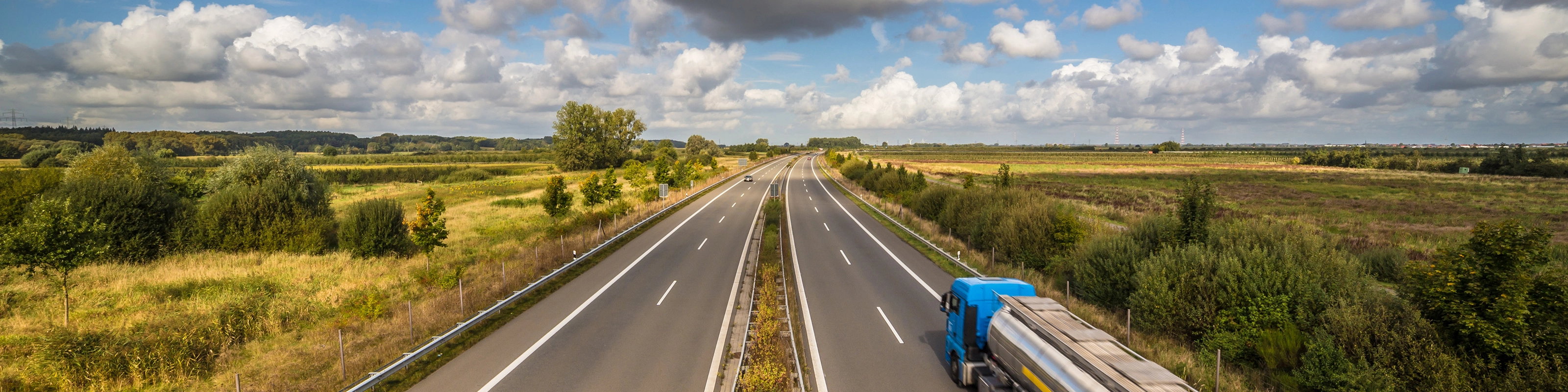 Tanklastwagen auf ländlicher Autobahn unter leicht bewölktem Himmel.