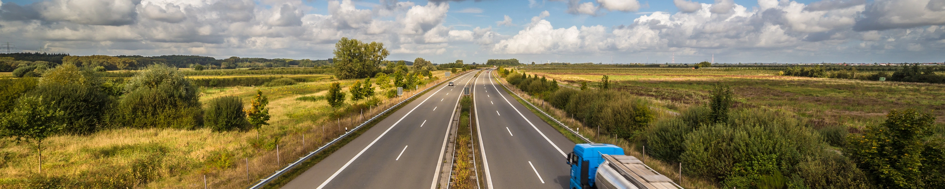 Tanklastwagen auf ländlicher Autobahn unter leicht bewölktem Himmel.