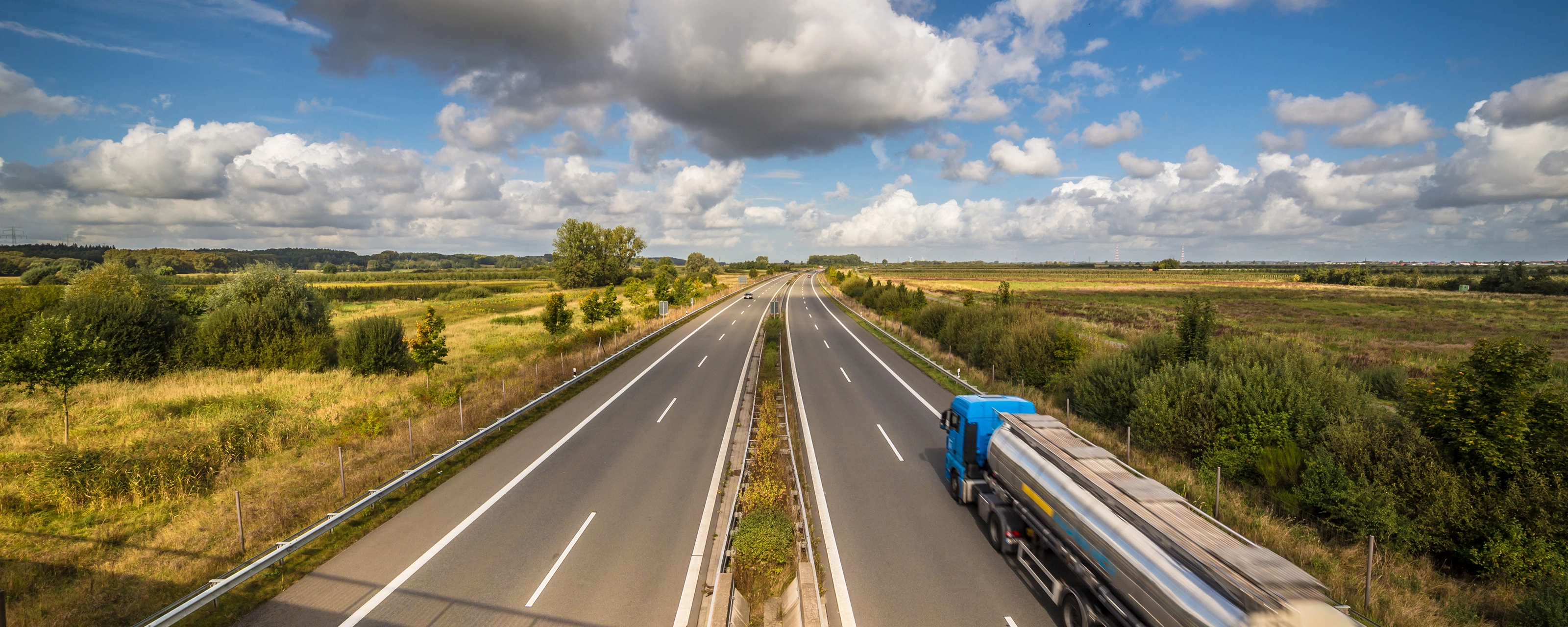 Tanklastwagen auf ländlicher Autobahn unter leicht bewölktem Himmel.