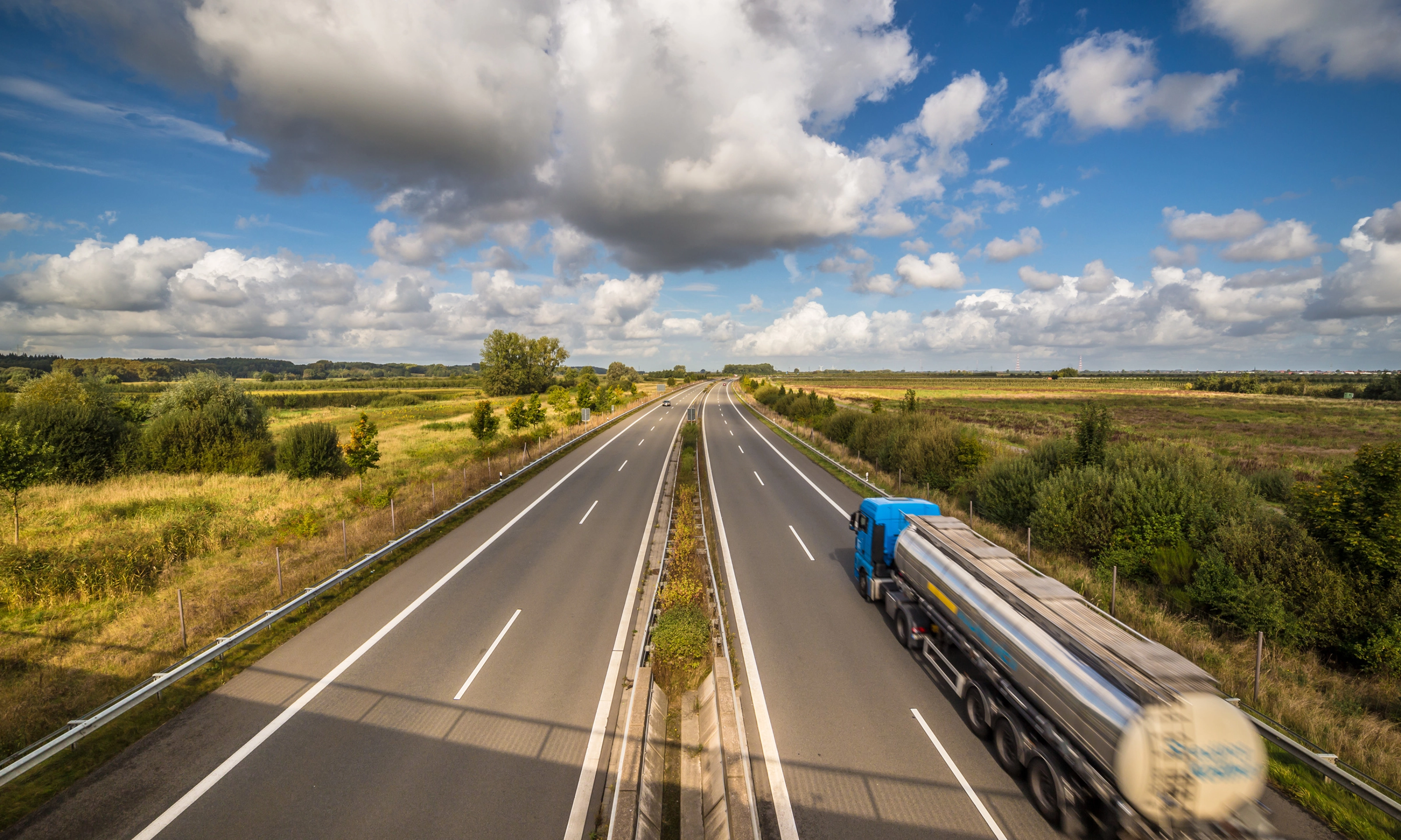 Tanklastwagen auf ländlicher Autobahn unter leicht bewölktem Himmel.
