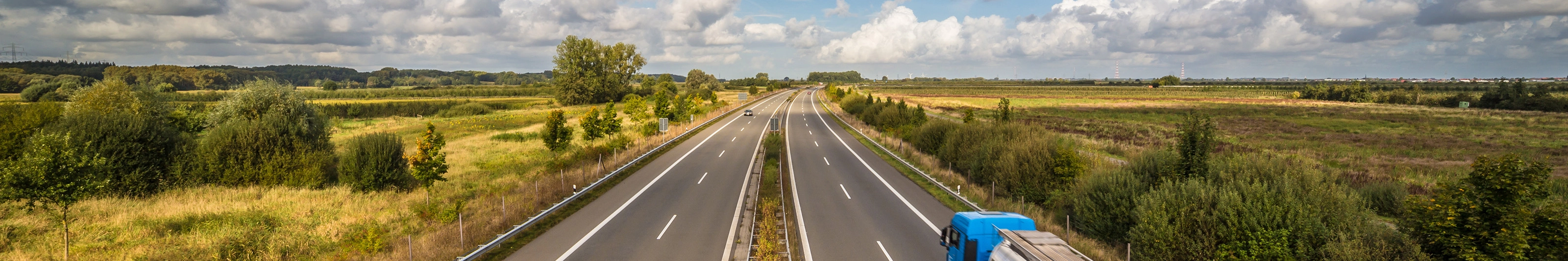 Tanklastwagen auf ländlicher Autobahn unter leicht bewölktem Himmel.