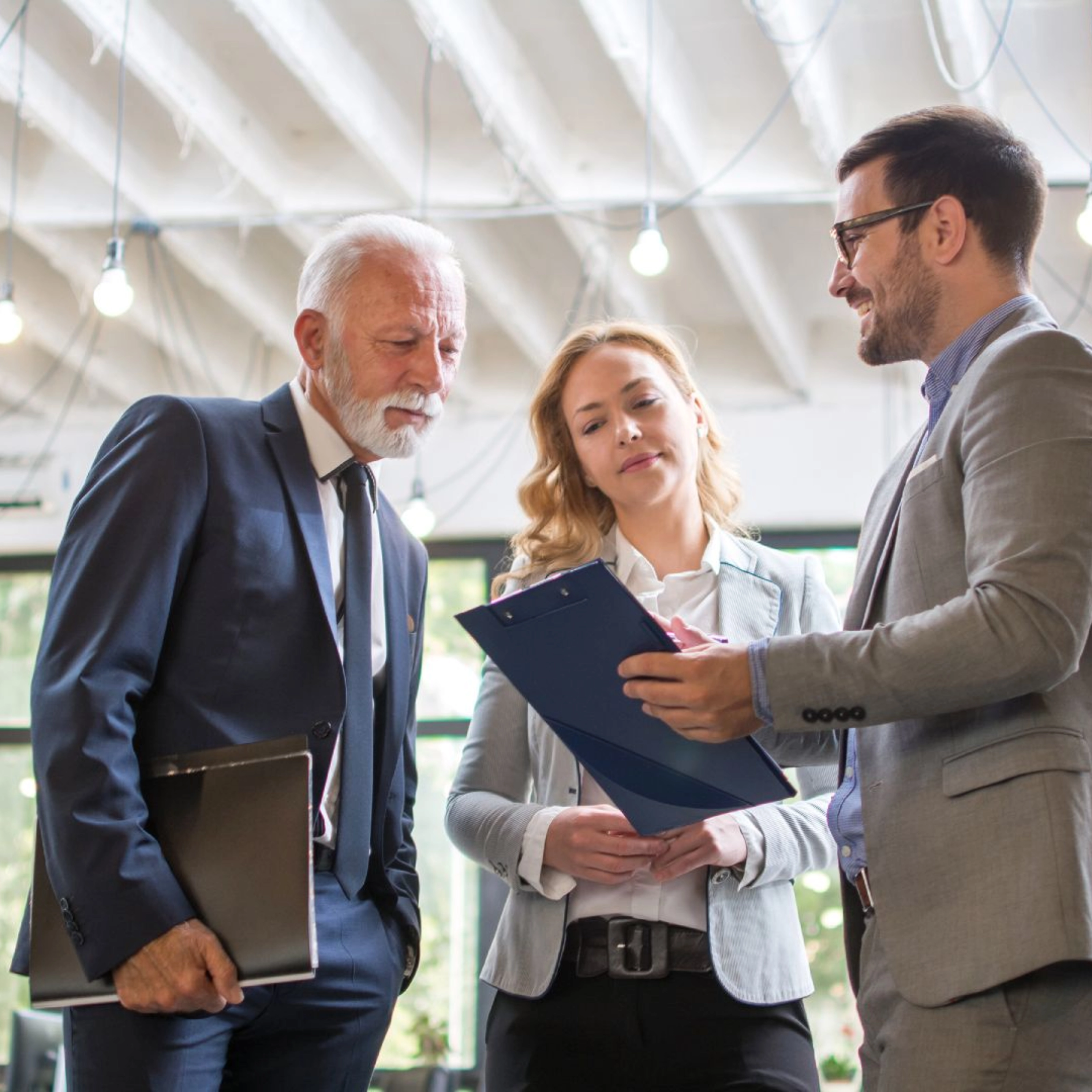 Drei Personen im Business-Outfit besprechen gemeinsam ein Dokument in einem modernen Büro.