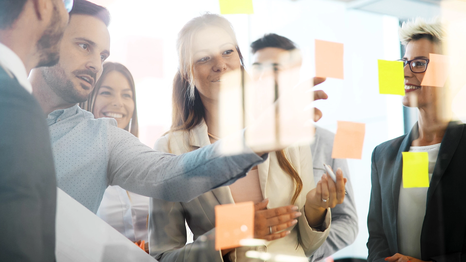 Group of people planning together in front of a glass wall with colorful sticky notes.