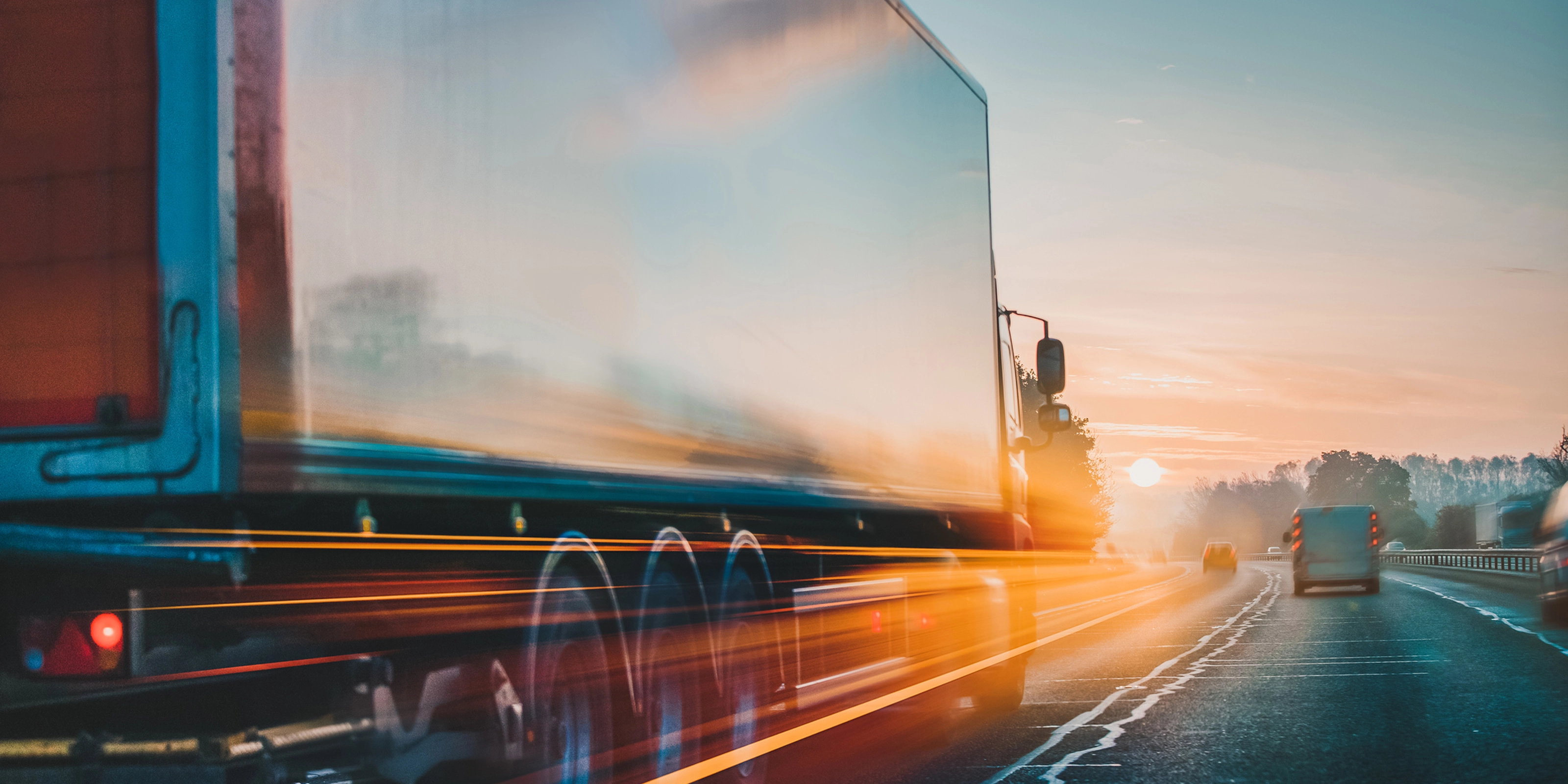 Lkw fährt bei Sonnenaufgang mit Lichtspuren und Bewegungsunschärfe auf der Autobahn.