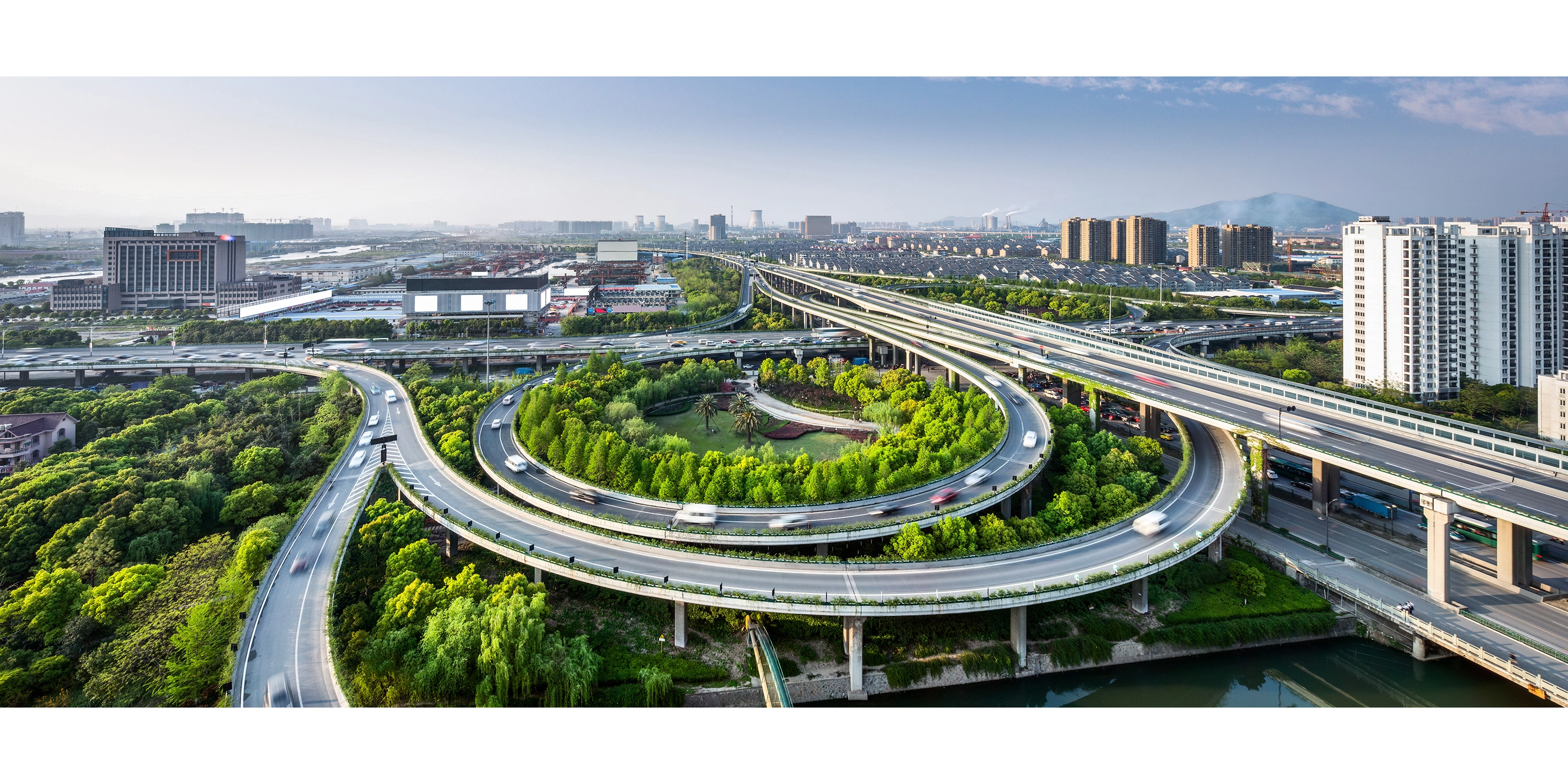 Großes Autobahnkreuz mit Schleifenauffahrten und Grünflächen in einer Stadtansicht.