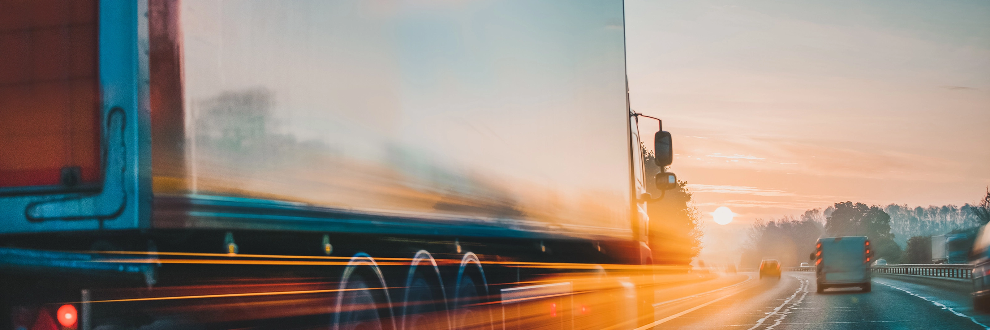 Lkw fährt bei Sonnenaufgang mit Lichtspuren und Bewegungsunschärfe auf der Autobahn.
