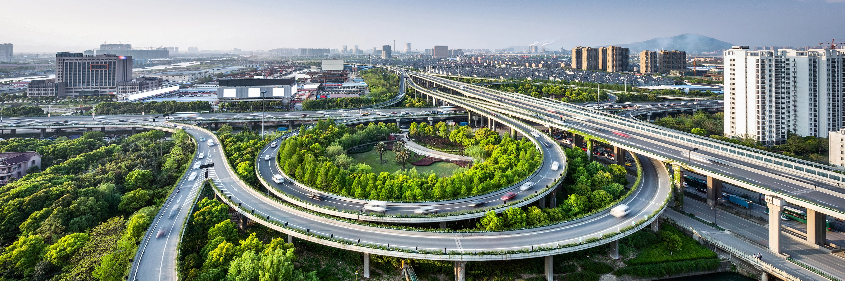 Großes Autobahnkreuz mit Schleifenauffahrten und Grünflächen in einer Stadtansicht.