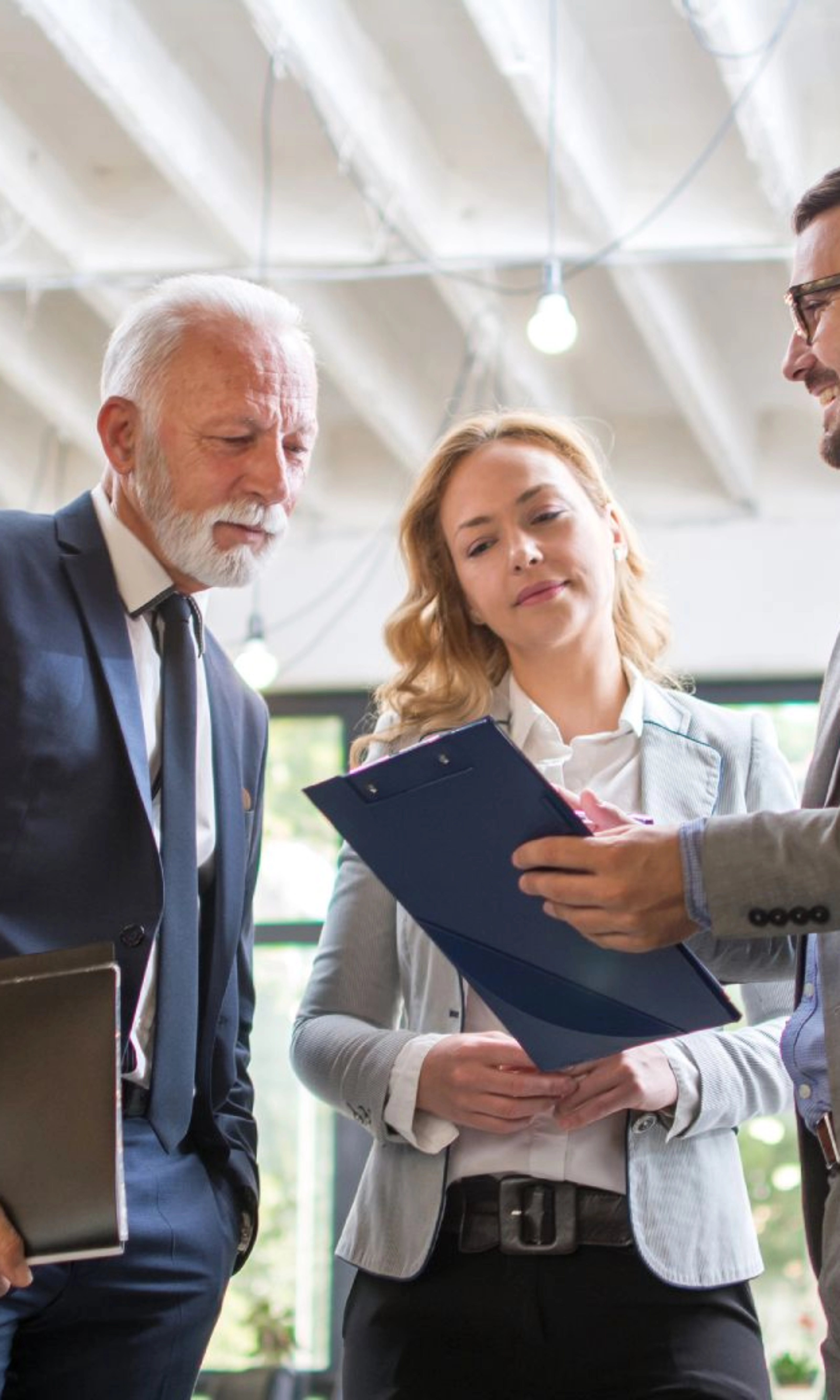 Drei Personen im Business-Outfit besprechen gemeinsam ein Dokument in einem modernen Büro.