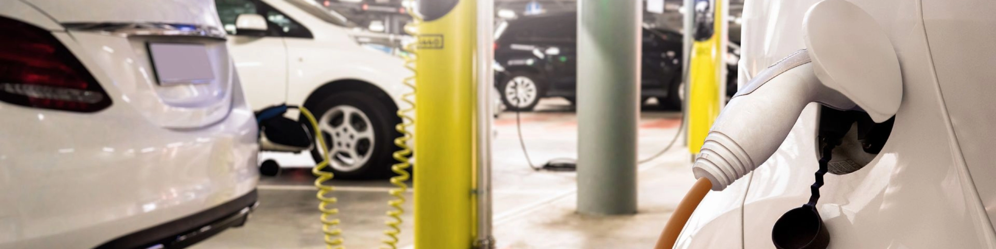 Electric cars charging at a yellow charging station in an indoor parking garage.