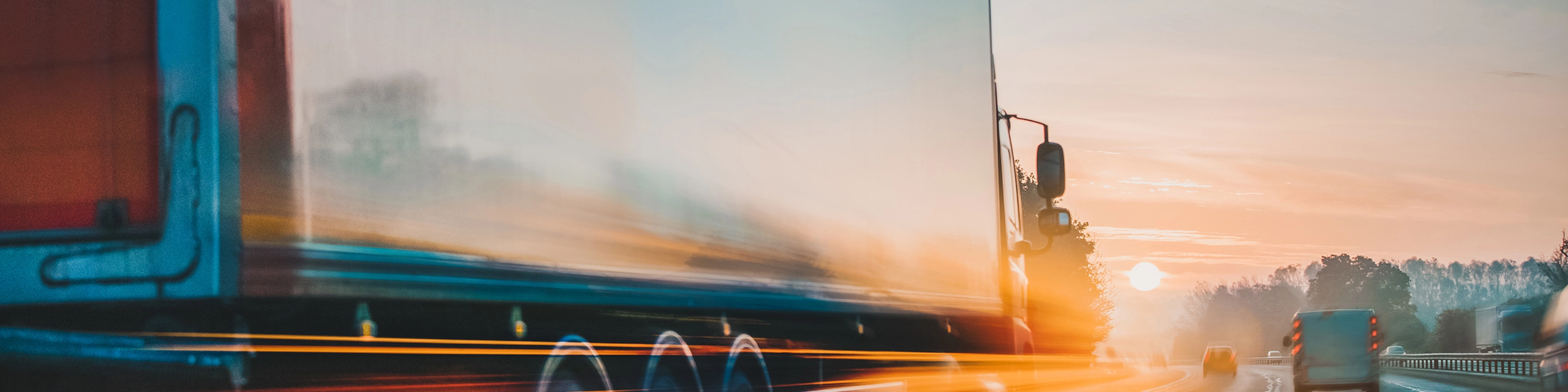 Lkw fährt bei Sonnenaufgang mit Lichtspuren und Bewegungsunschärfe auf der Autobahn.