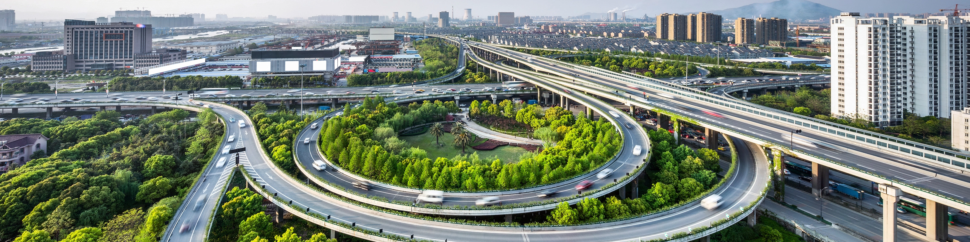 Großes Autobahnkreuz mit Schleifenauffahrten und Grünflächen in einer Stadtansicht.