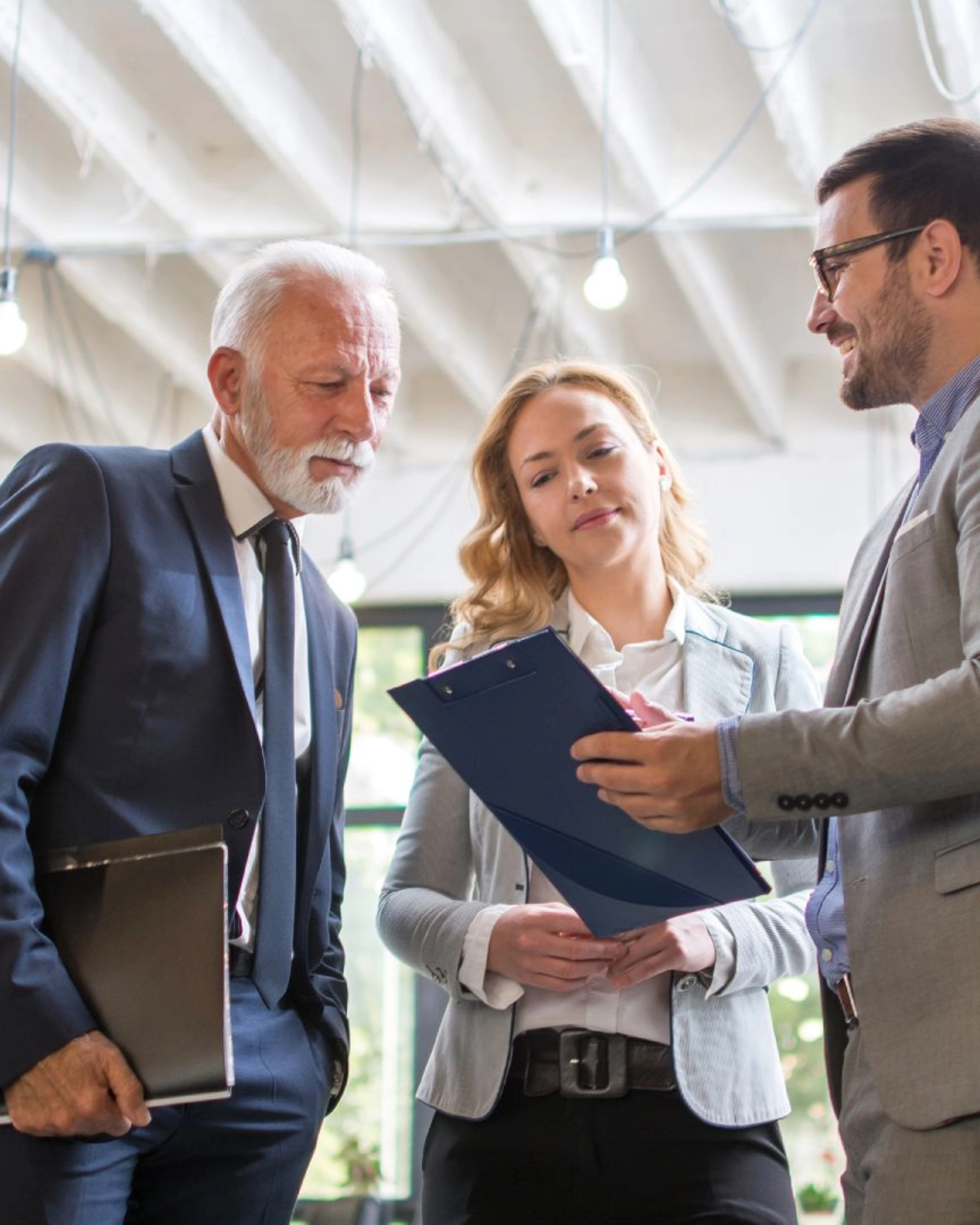 Drei Personen im Business-Outfit besprechen gemeinsam ein Dokument in einem modernen Büro.