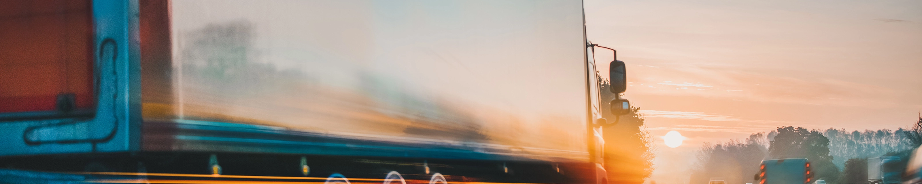 Lkw fährt bei Sonnenaufgang mit Lichtspuren und Bewegungsunschärfe auf der Autobahn.