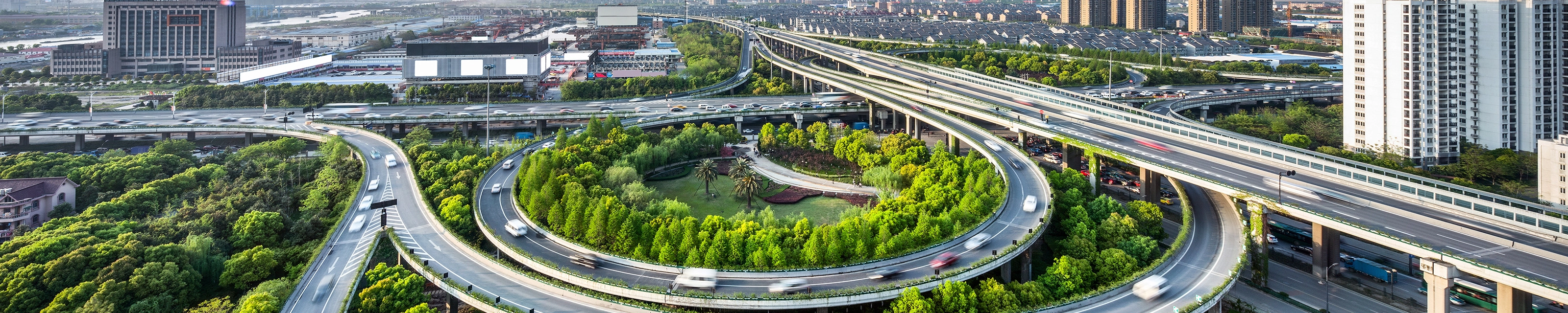 Großes Autobahnkreuz mit Schleifenauffahrten und Grünflächen in einer Stadtansicht.