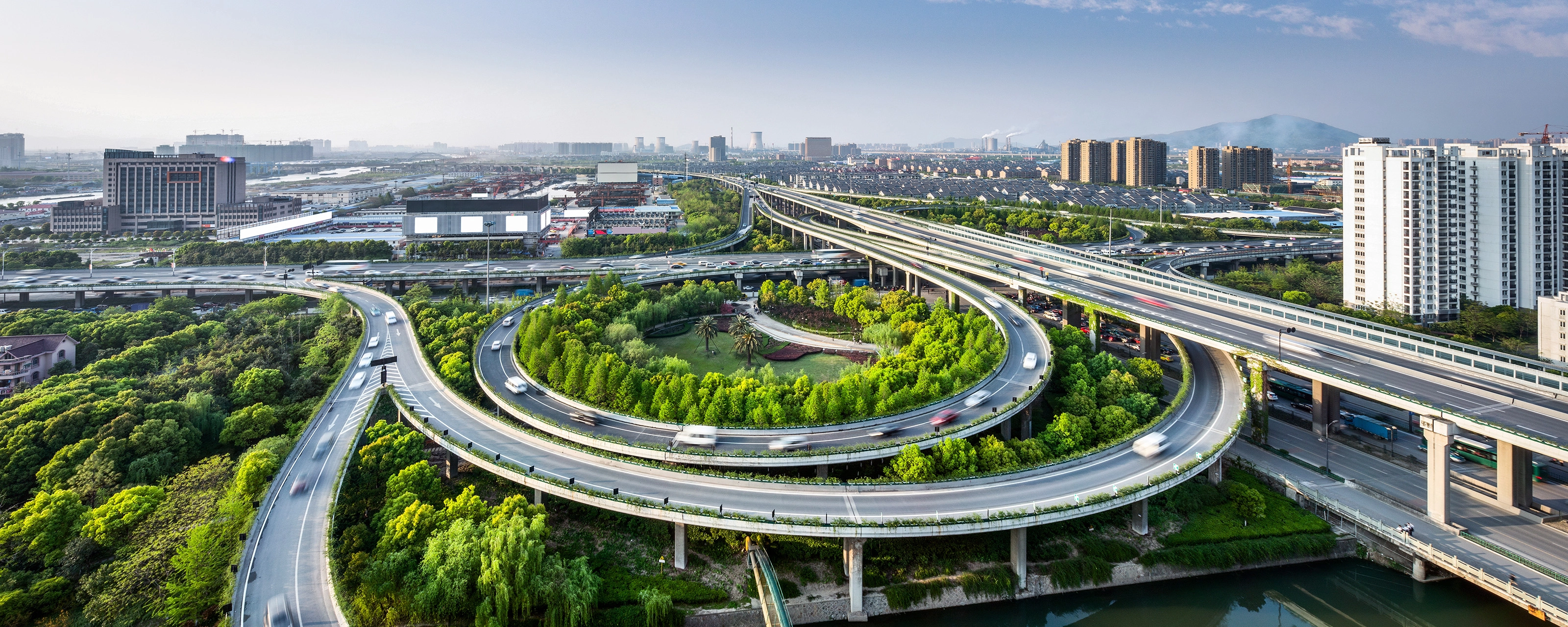 Großes Autobahnkreuz mit Schleifenauffahrten und Grünflächen in einer Stadtansicht.
