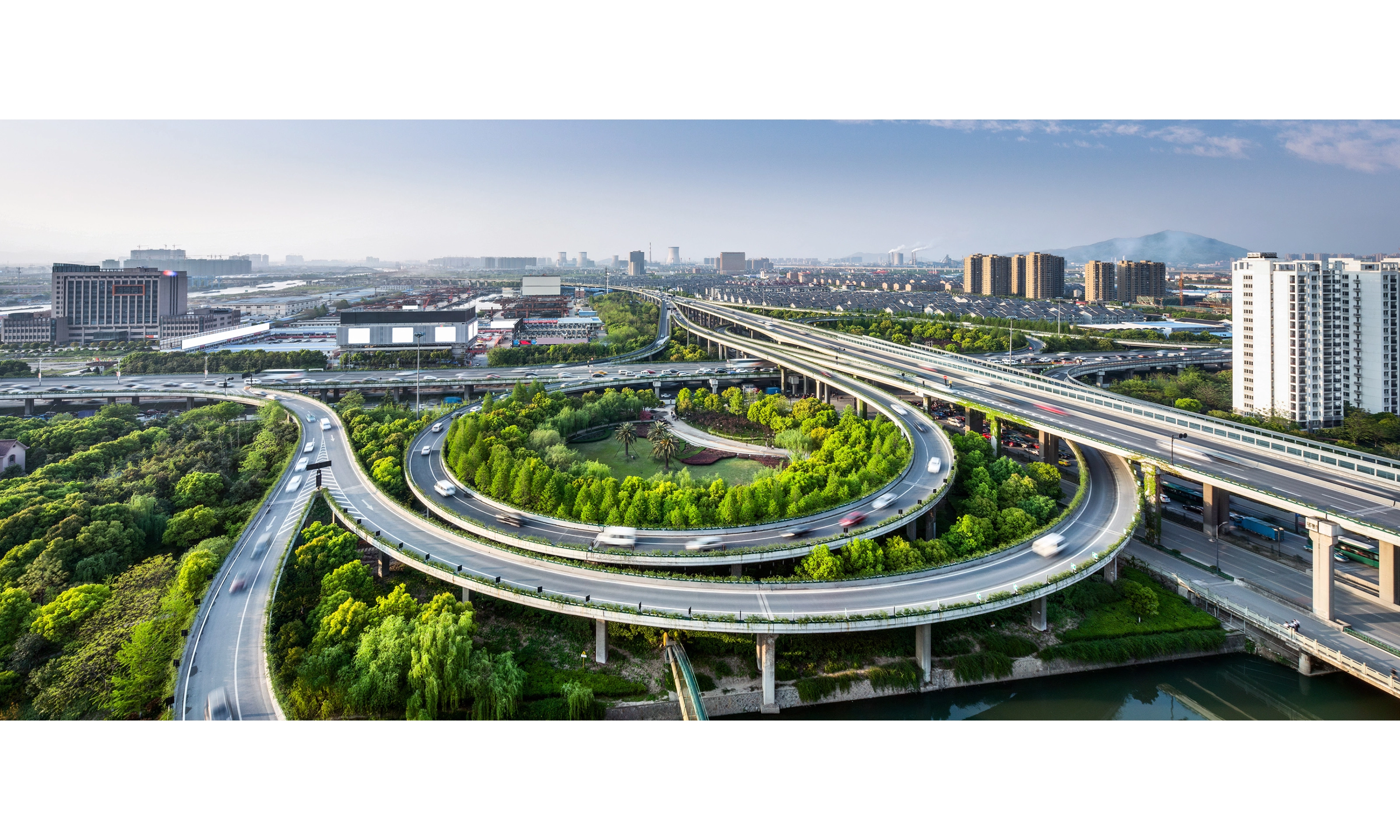 Großes Autobahnkreuz mit Schleifenauffahrten und Grünflächen in einer Stadtansicht.