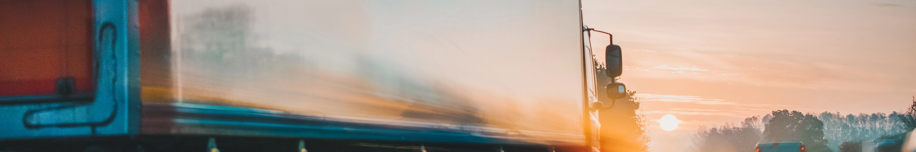 Lkw fährt bei Sonnenaufgang mit Lichtspuren und Bewegungsunschärfe auf der Autobahn.