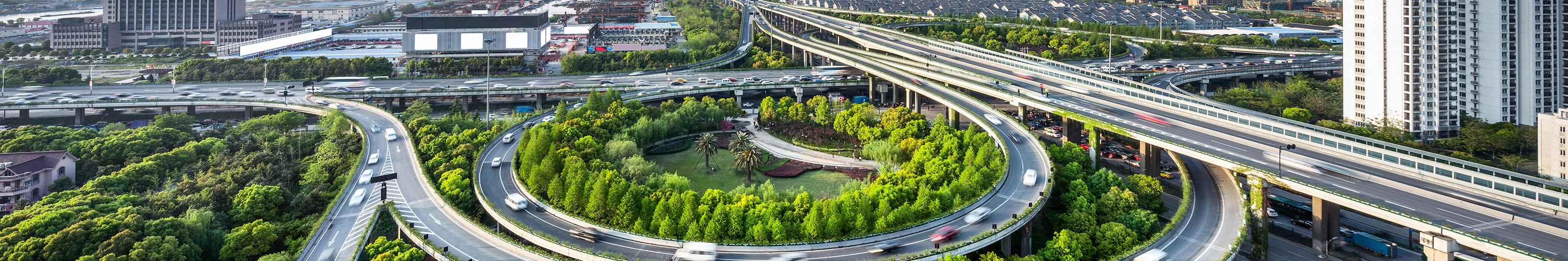 Großes Autobahnkreuz mit Schleifenauffahrten und Grünflächen in einer Stadtansicht.