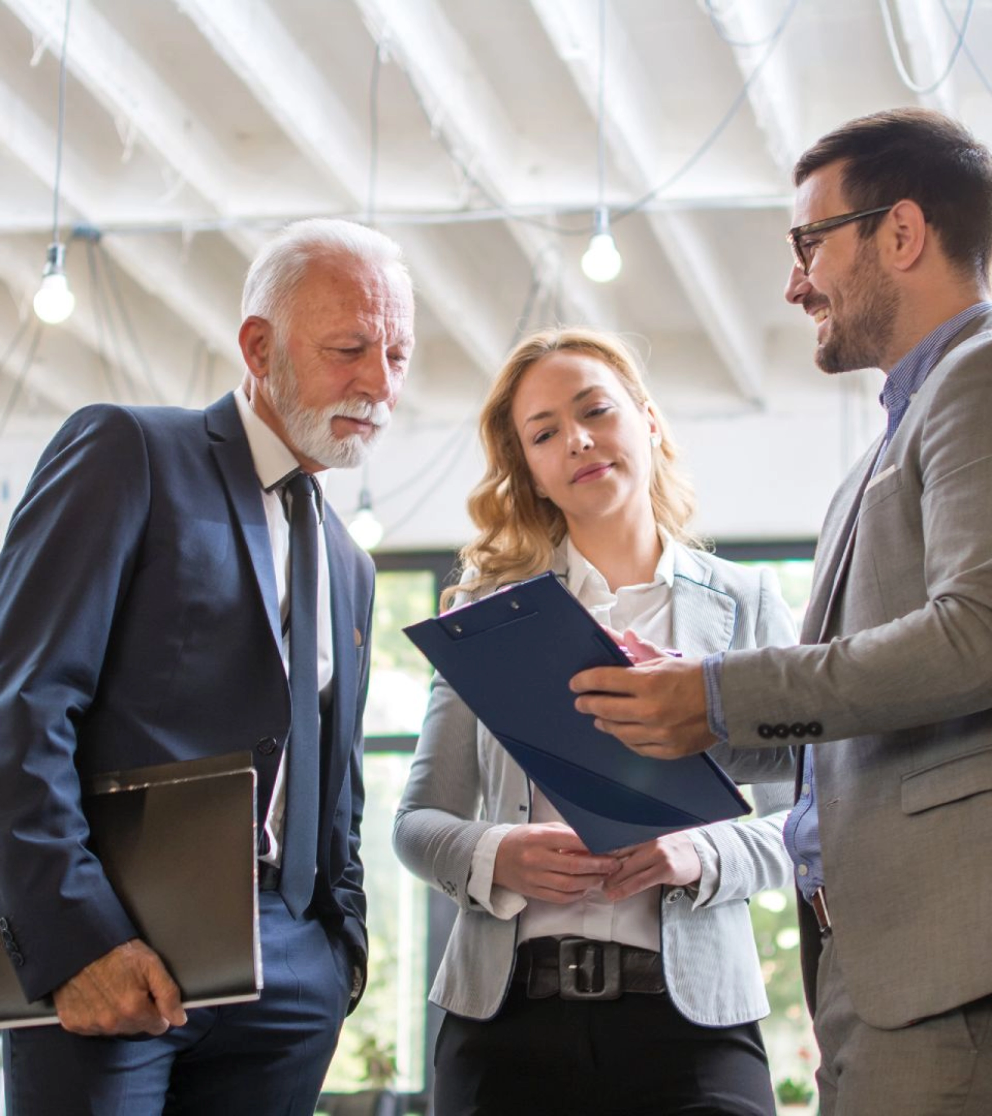 Drei Personen im Business-Outfit besprechen gemeinsam ein Dokument in einem modernen Büro.
