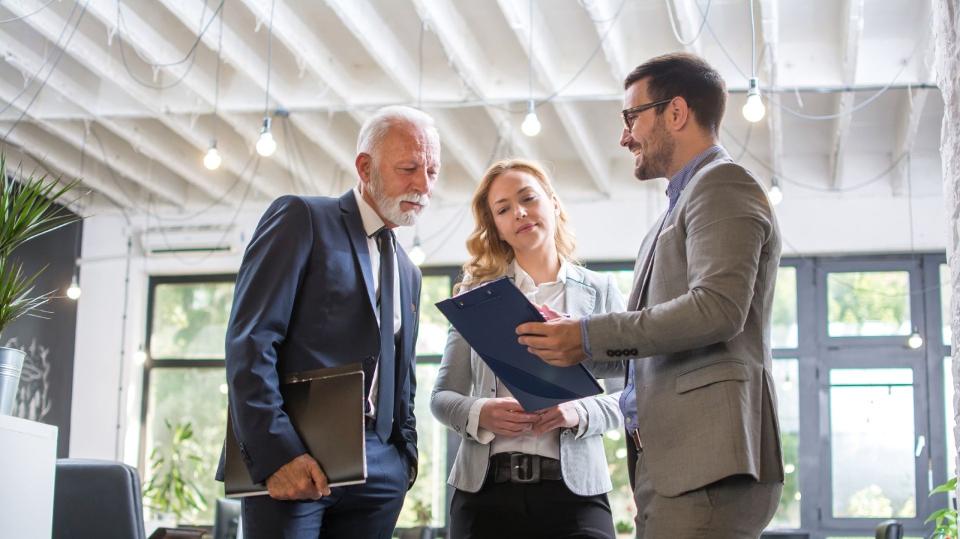 Drei Personen im Business-Outfit besprechen gemeinsam ein Dokument in einem modernen Büro.