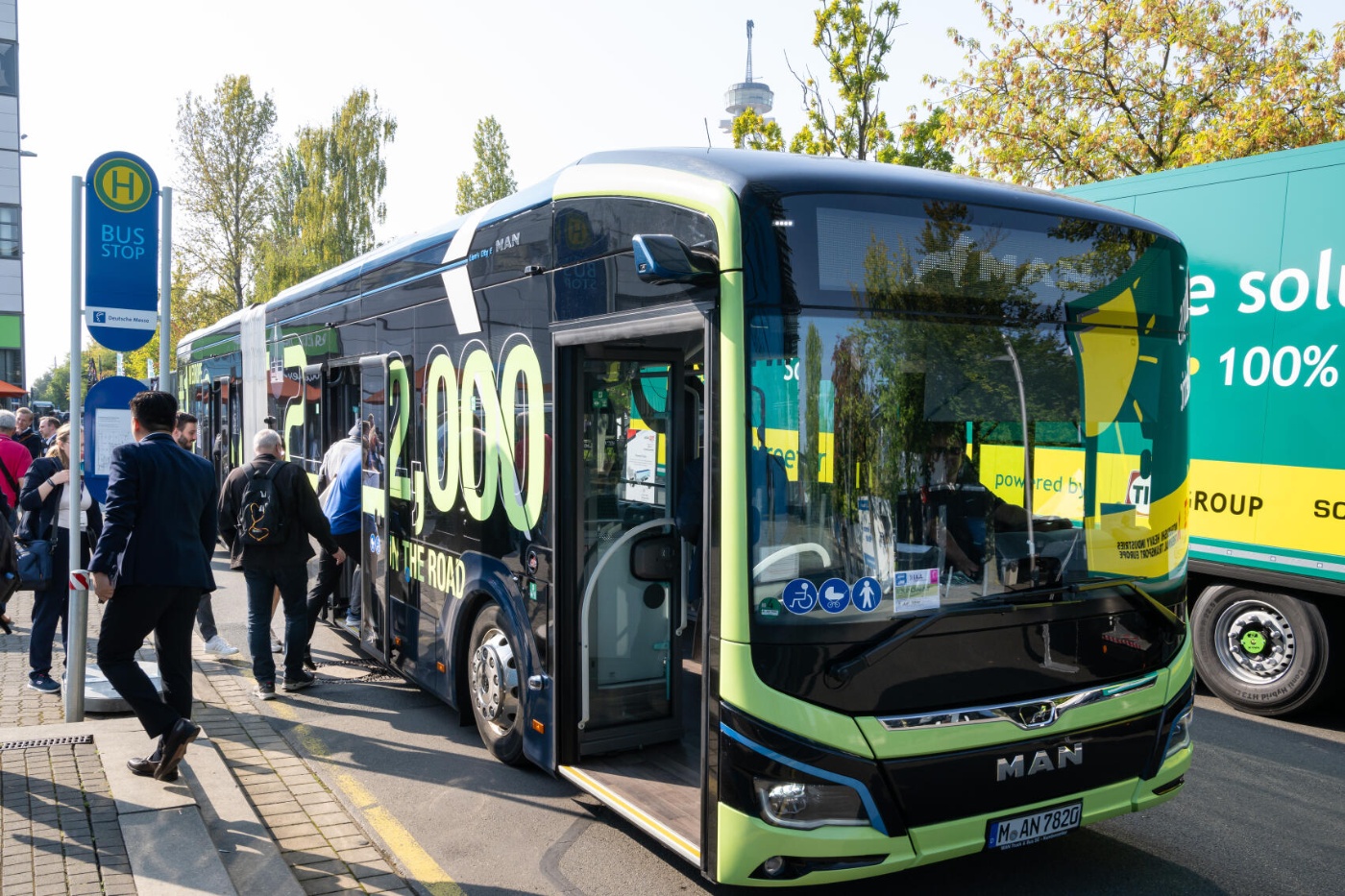 Menschen steigen bei der IAA Transportation an einer Haltestelle in einen modernen MAN-Shuttlebus ein.
